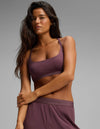 A woman with long dark hair wears the Cozy Earth Women’s First Layer Soft Bra and matching shorts, standing against a plain gray background while looking slightly to the side with a relaxed expression.|Color:Fig