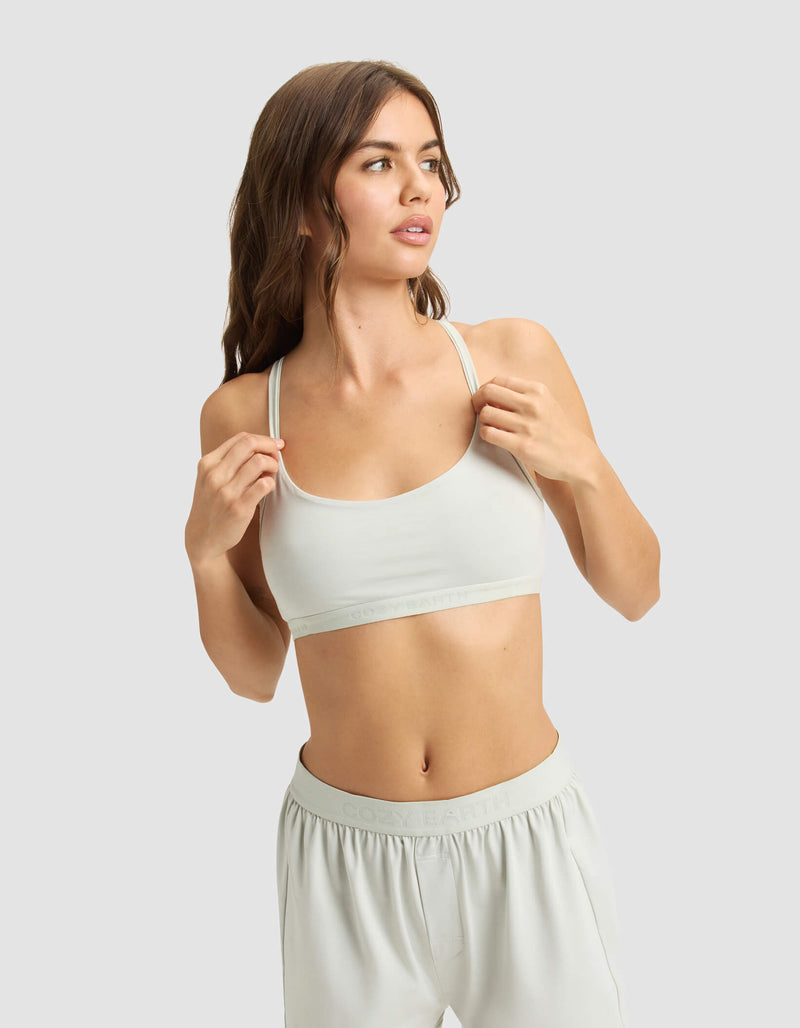 A woman with long brown hair models the Cozy Earth Women's First Layer PJ Soft Bra and matching shorts, standing against a plain light gray background and looking to the side.