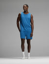 A man stands in a studio against a plain gray background wearing the Cozy Earth Men’s First Layer Pajama Tank & Short Set in blue, paired with white socks and white shoes.|Color:Anchor