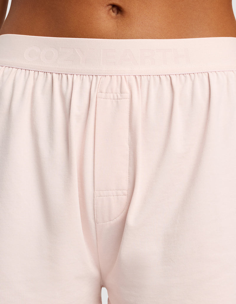 A close-up of a person wearing Cozy Earth Women's First Layer Pajama Boxer Short in light pink, featuring an elastic waistband with "COZY EARTH" embossed and a small front pocket.