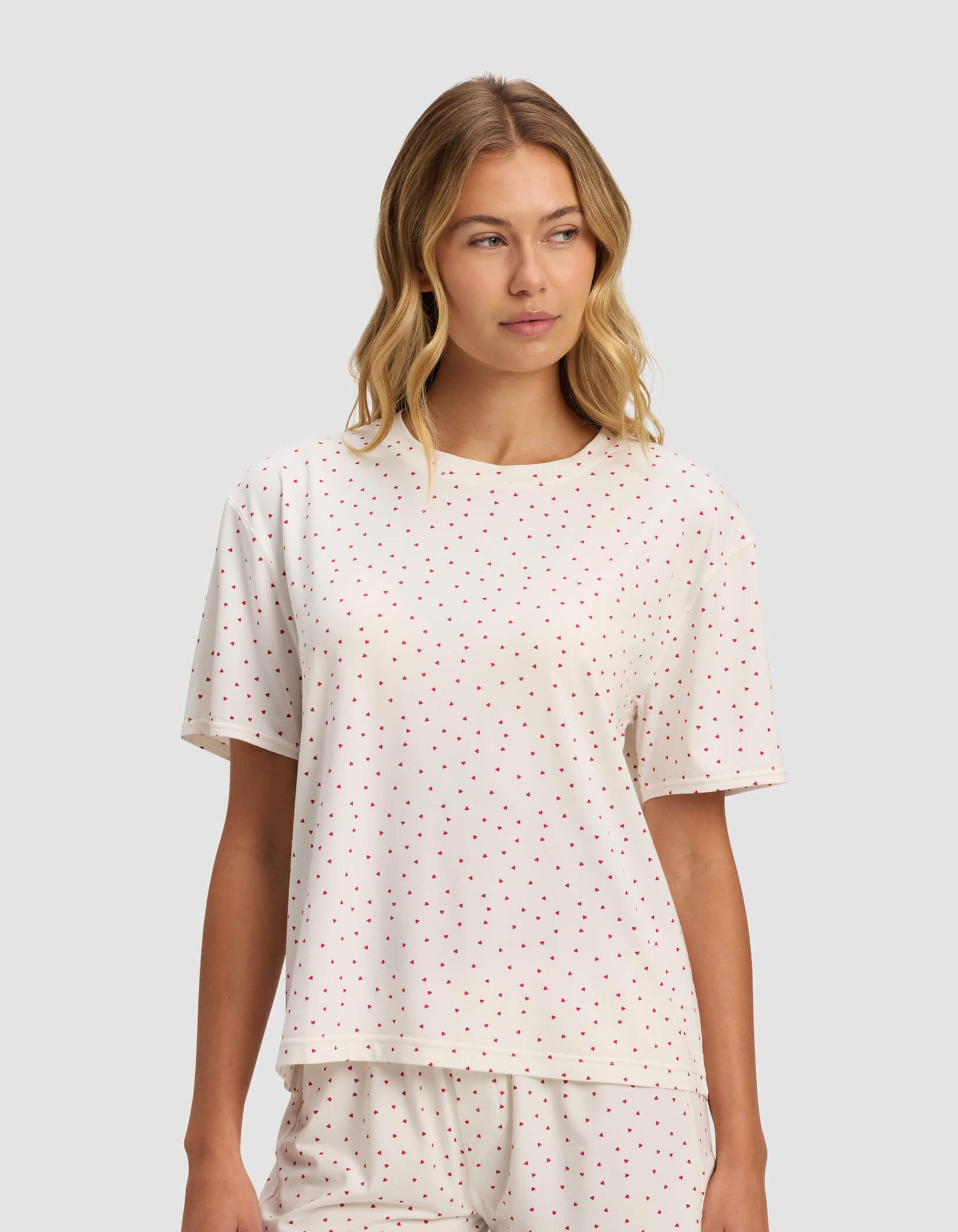 A woman wears the Cozy Earth Women's First Layer Pajama Short Sleeve Tee set with white fabric and small red polka dots, including a short-sleeve top and shorts, standing against a light gray background.