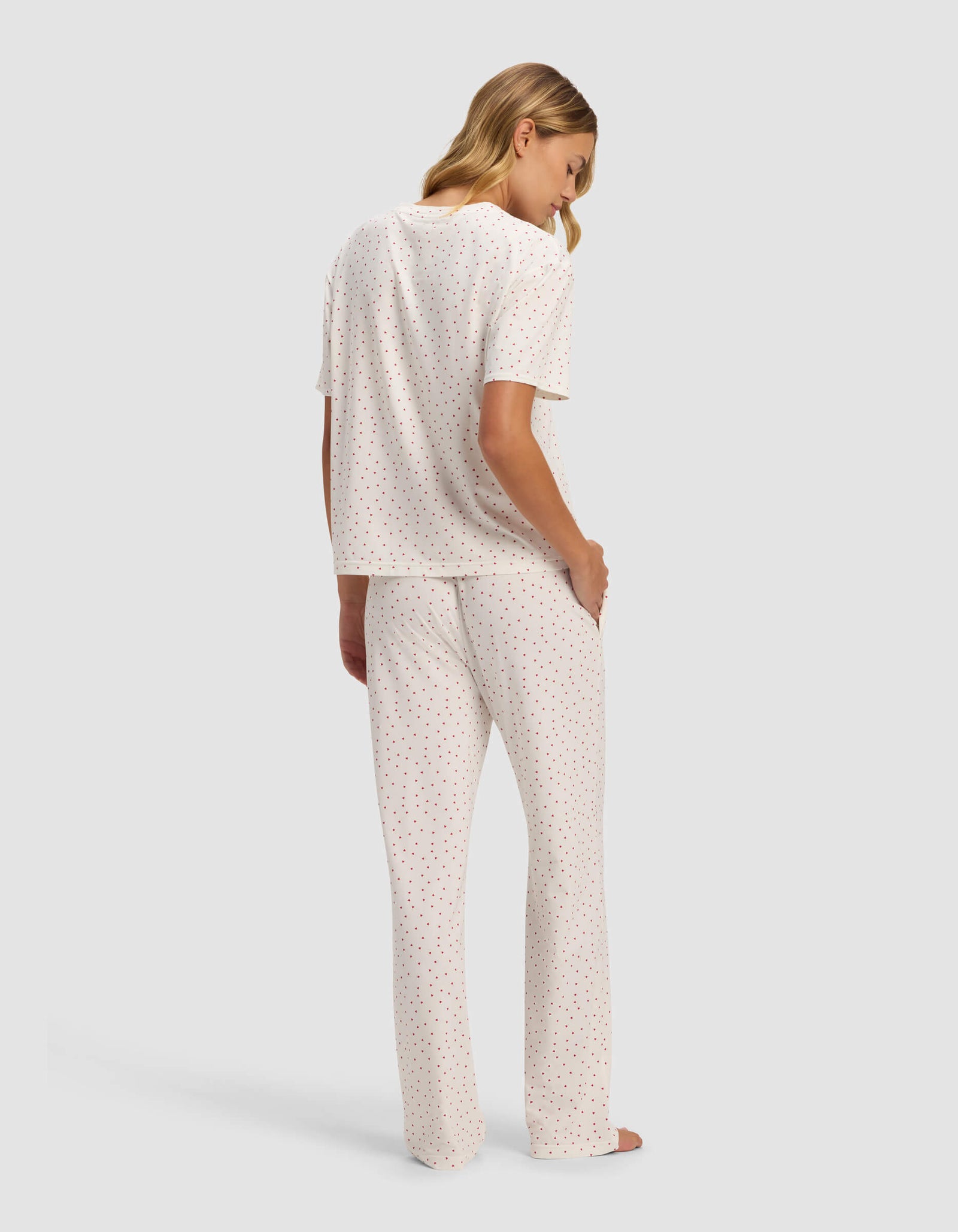 A blonde woman stands barefoot, facing away, wearing the Cozy Earth Women's First Layer Pajama Short Sleeve Tee & Pant Set in white with a small, colorful polka dot pattern.