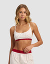 A woman models the Cozy Earth Women's First Layer Pajama Soft Bra set, featuring a white base with small red polka dots, red waistband on the shorts, and a red band on the bralette, against a light gray background.|Color:Cranberry Sea Salt Mini Heart