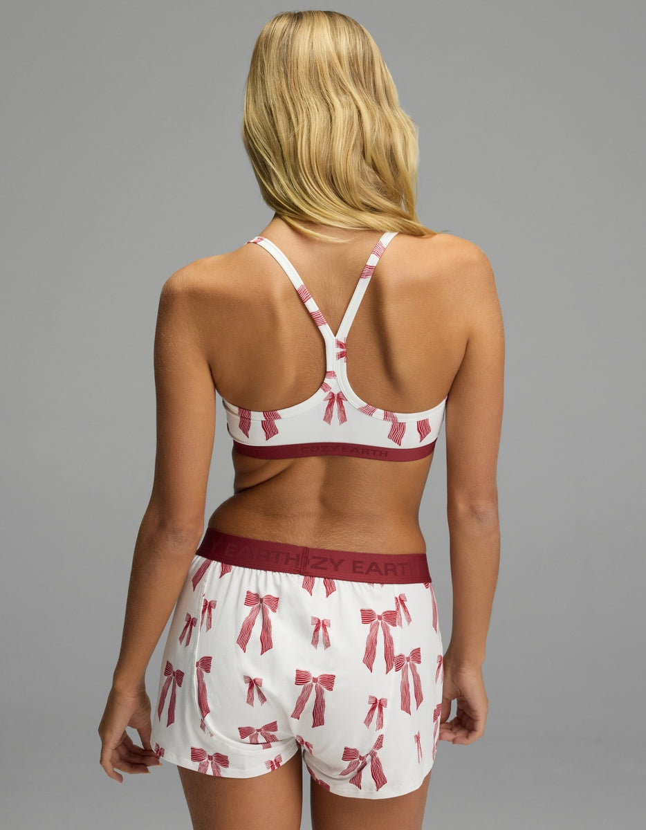 Back view of a person wearing a white Cozy Earth Women’s First Layer Soft Bra racerback bralette and shorts with a red bow print and maroon branded elastic bands.