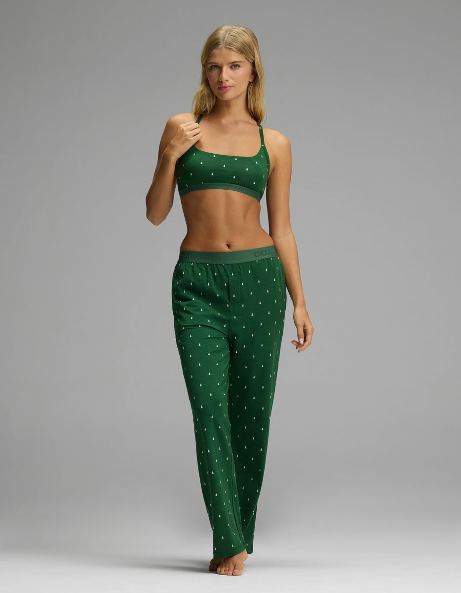 A woman wearing a dark green Cozy Earth Women’s First Layer Soft Bra and matching pajama pants with a small white tree print.