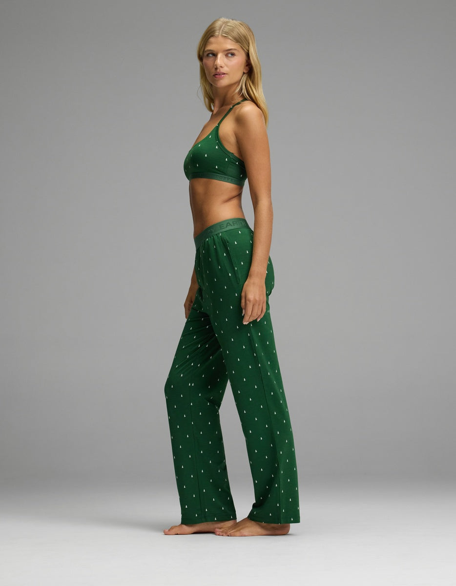A woman wearing a dark green Women’s First Layer Pajama Soft Bra & Pajama Pant Set featuring a matching bralette and lounge pants with a small white tree print.