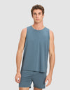 A young man with short, curly brown hair wears the Cozy Earth Men's First Layer Pajama Tank in blue, paired with matching shorts, standing against a plain light gray background and looking directly at the camera.|Color:Dawn