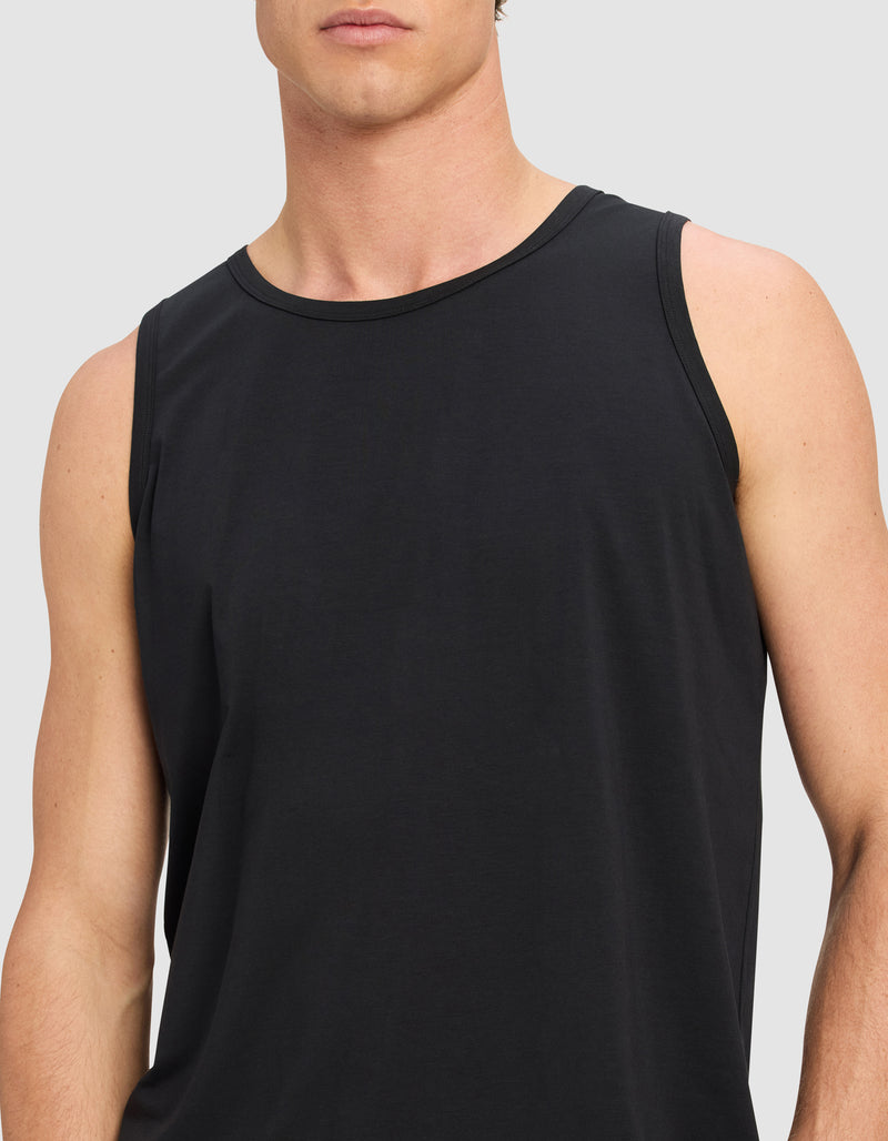 A model wears the Cozy Earth Men's First Layer Pajama Tank in black, shown from shoulders to waist against a plain light gray background. The person's face is partially out of frame.