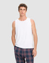 A man wears the Cozy Earth Men's First Layer Pajama Tank in white, paired with blue plaid pants, standing against a light gray background and looking directly at the camera with a neutral expression.|Color:White