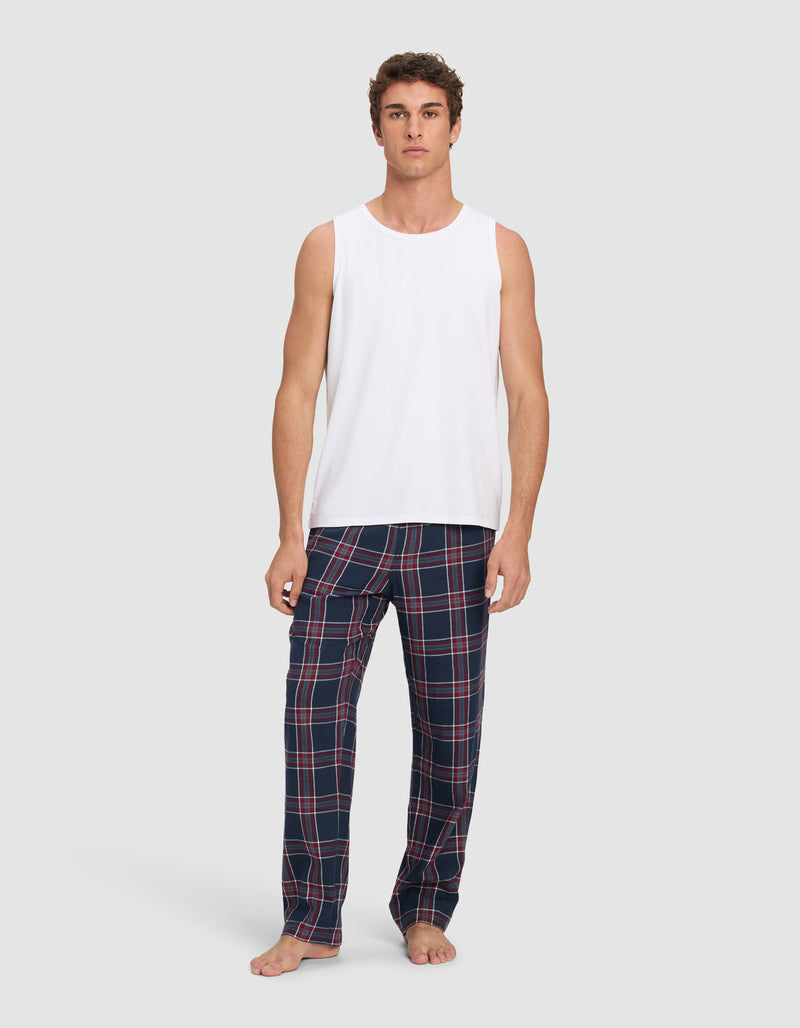 A man stands barefoot against a plain background, wearing the Cozy Earth Men's First Layer Pajama Tank and blue plaid pajama pants with red and white lines.