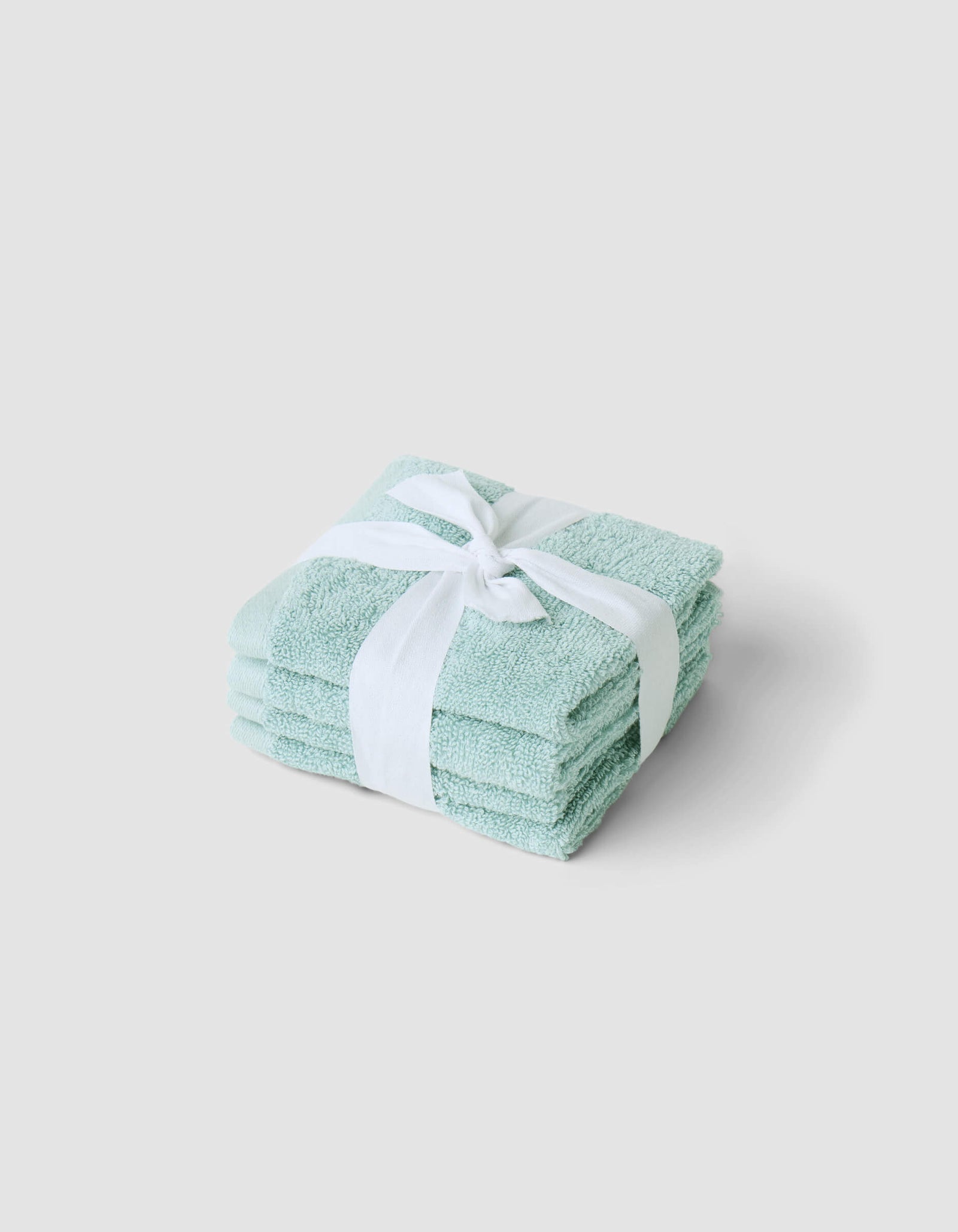 A neatly folded stack of Cozy Earth Complete Cleansing Cloths, tied with a white ribbon and placed on a plain light gray background.