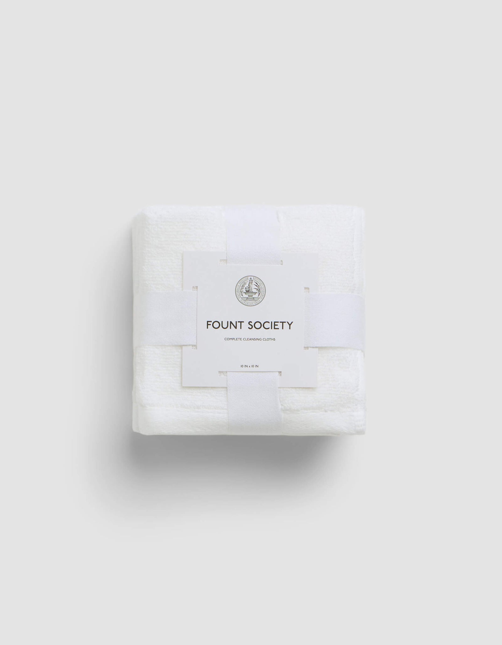 A neatly folded white Complete Cleansing Cloth by Cozy Earth, wrapped with a white paper band featuring the brand name and a small circular logo, set against a plain light gray background.