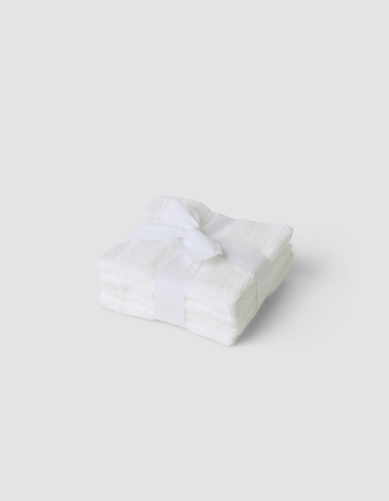 A stack of three folded Cozy Earth Complete Cleansing Cloths, tied with a white ribbon and set against a plain light gray background.