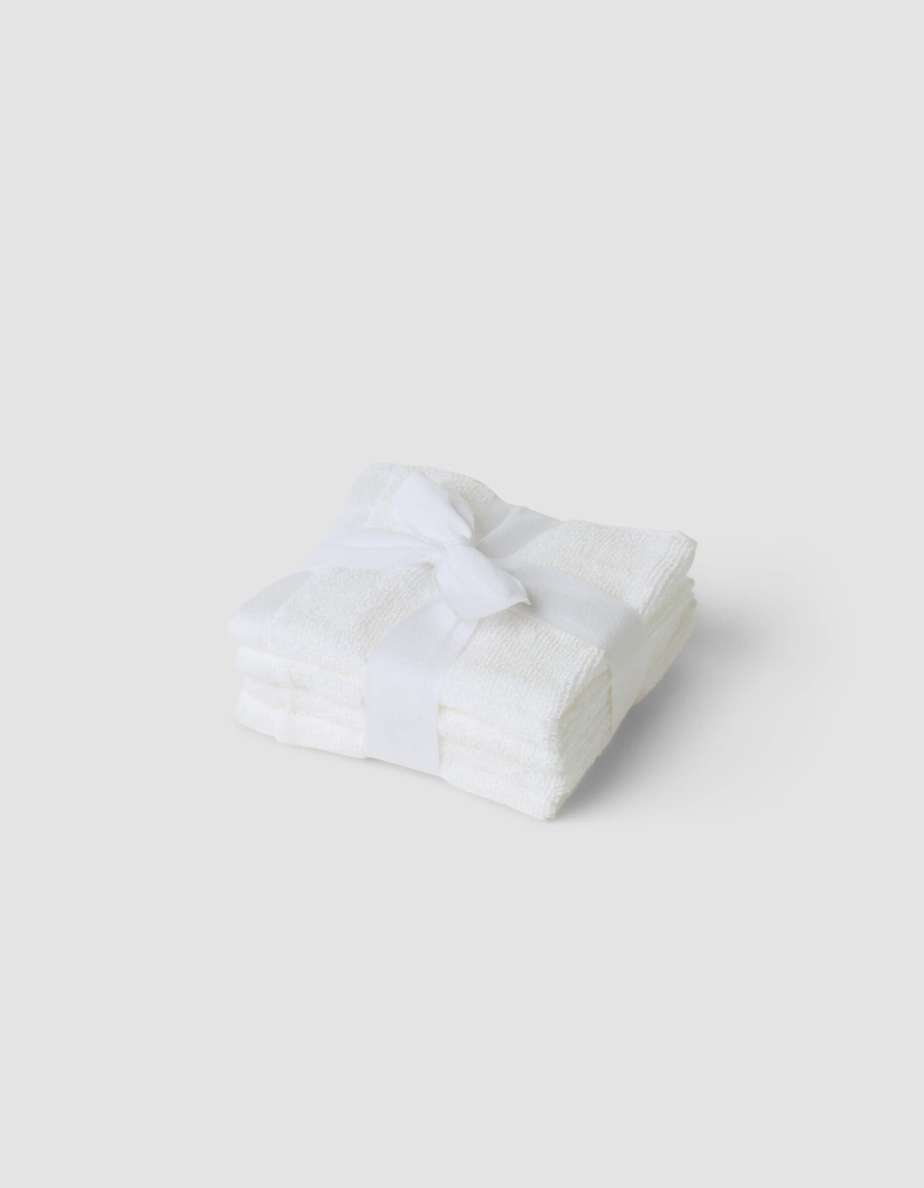 A stack of three folded Cozy Earth Complete Cleansing Cloths, tied with a white ribbon and set against a plain light gray background.