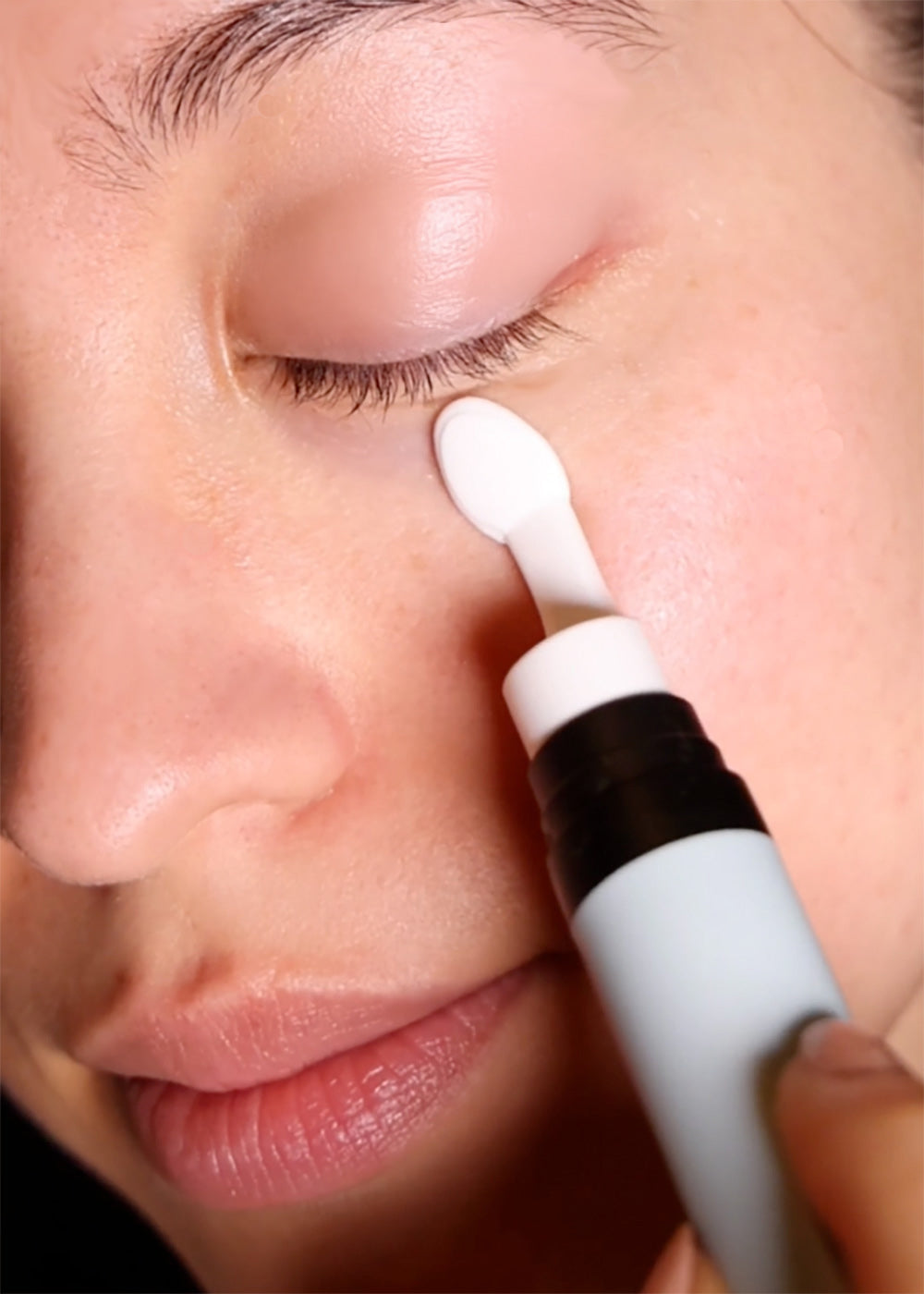 A close-up shows a person applying Cozy Earth Eye Cream under their eye with a white applicator. Their eyes are closed, and their skin looks smooth and hydrated.