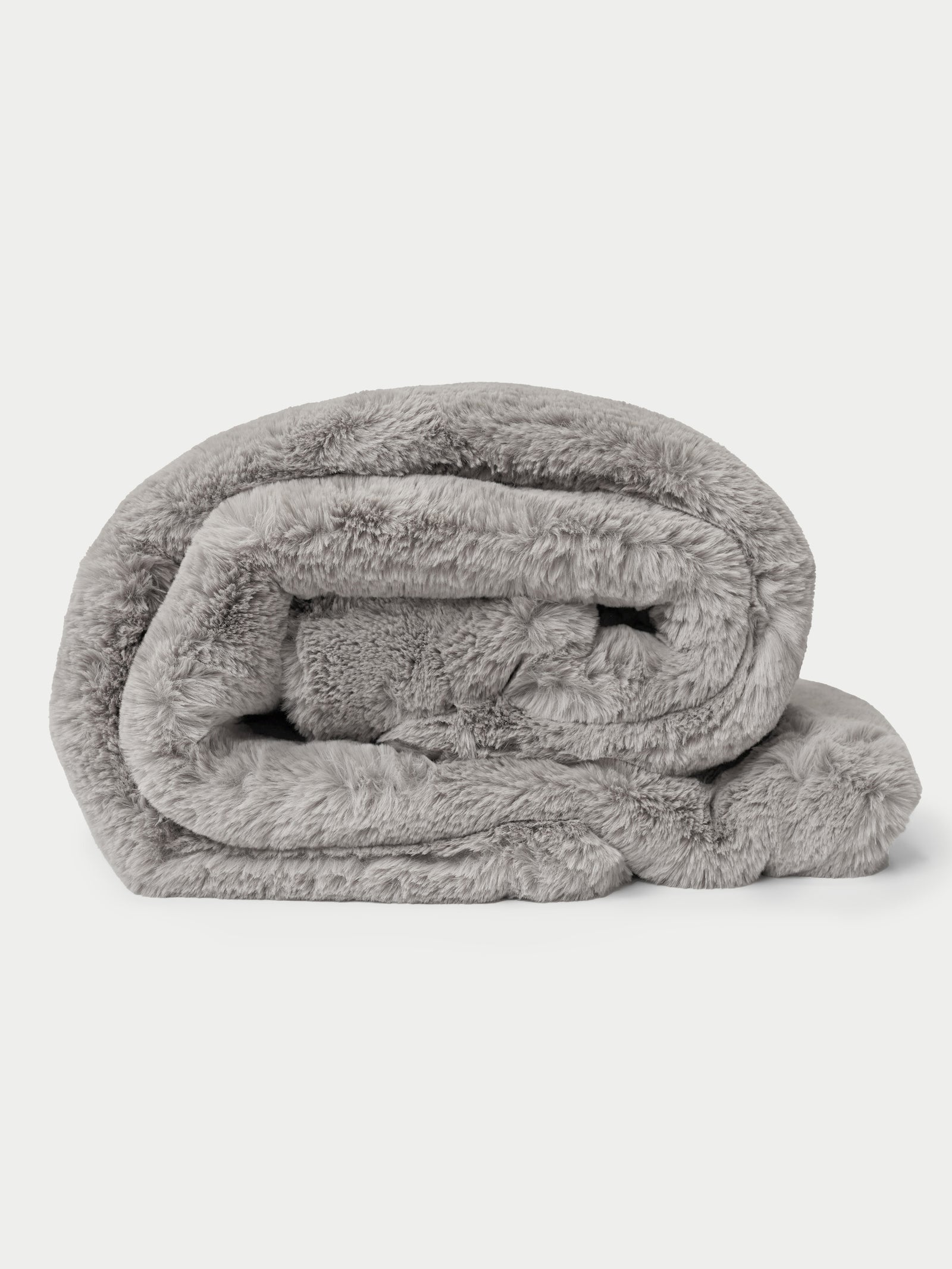 A rolled-up, plush Cuddle Blanket from Cozy Earth in gray faux fur on a plain white background. 