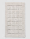 The Cozy Earth Grid Bath Mat is a rectangular, off-white mat with a raised grid design and a thick, fluffy border.|Color:Light Grey