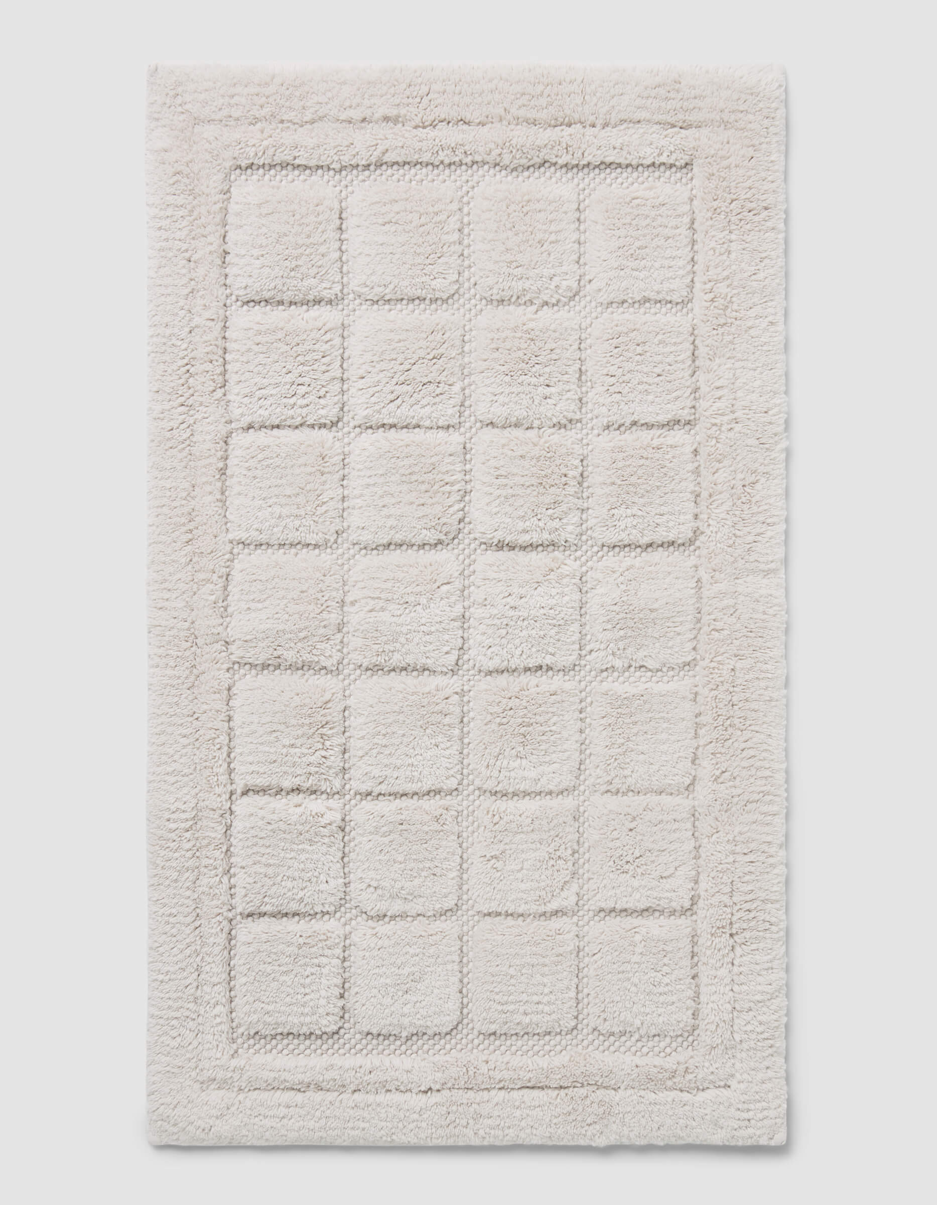 The Cozy Earth Grid Bath Mat is a rectangular, off-white mat with a raised grid design and a thick, fluffy border.|Color:Light Grey