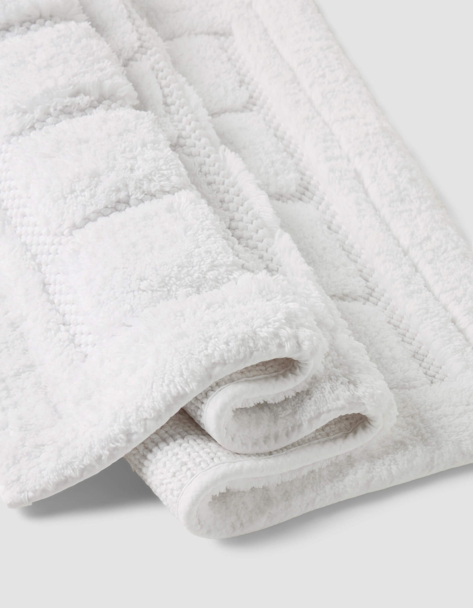 A close-up of the Folded Grid Bath Mat by Cozy Earth, featuring a white textured geometric pattern, displayed on a light gray background.