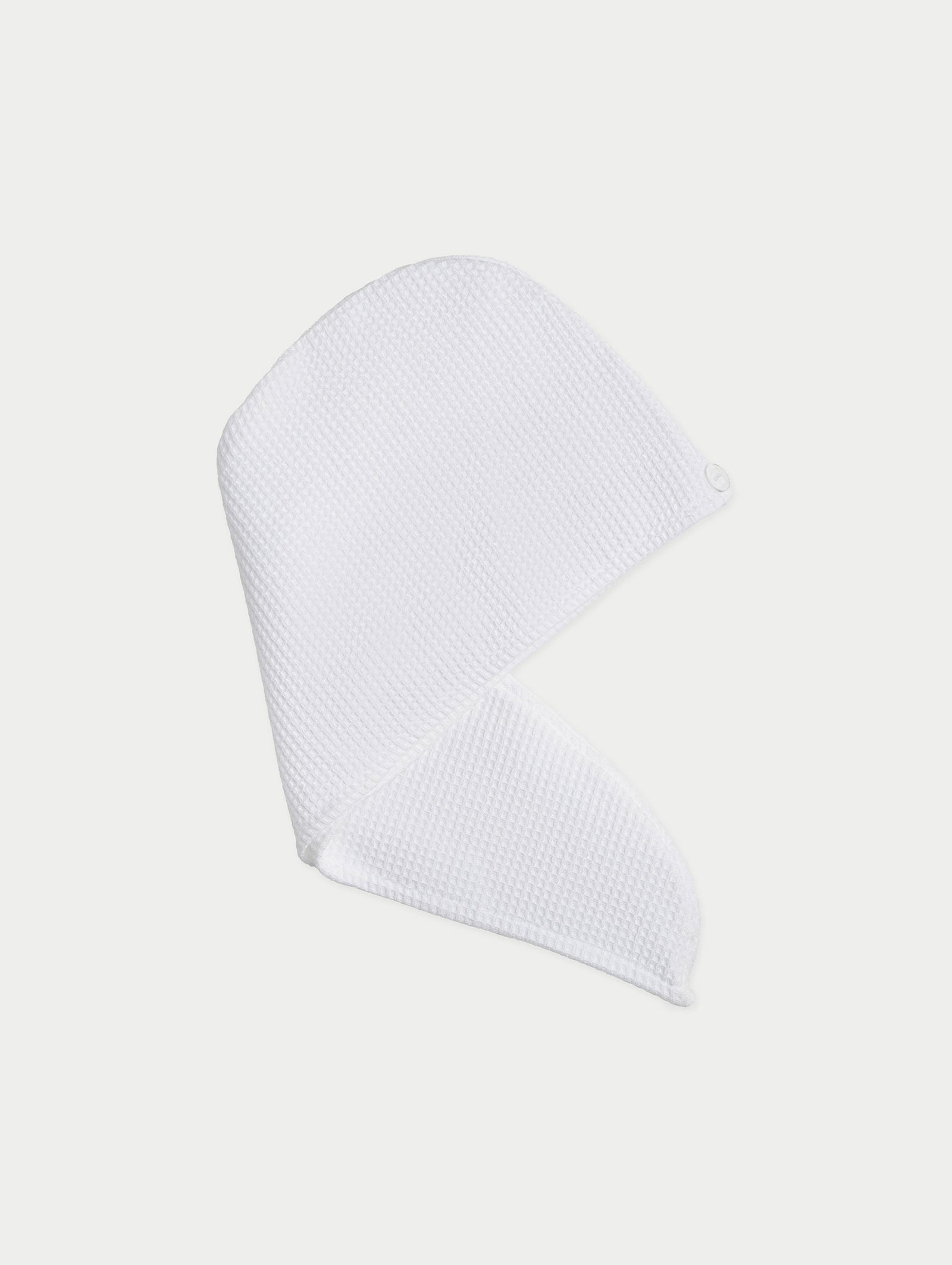 The At-Home Spa Bundle by Cozy Earth includes a white, textured towel wrap for hair with a button closure, displayed against a light background to highlight its smooth, waffle-like fabric.