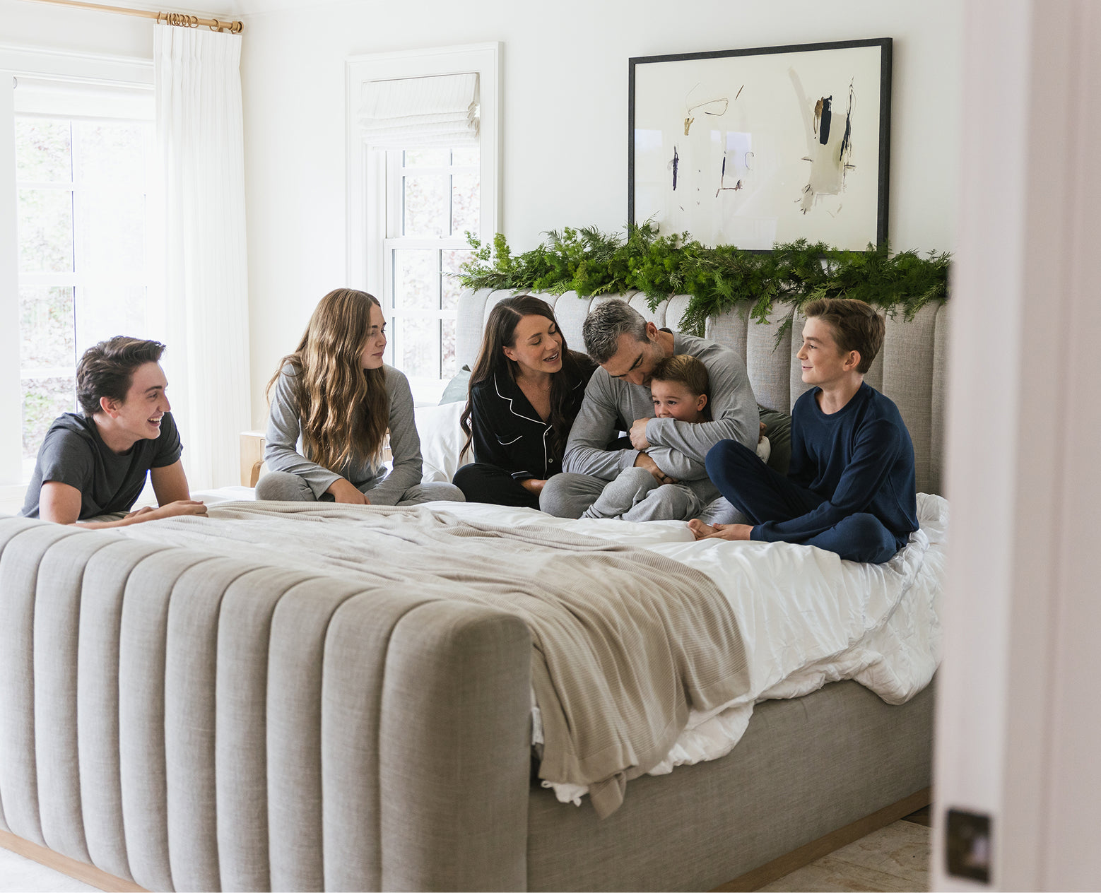 Family sitting on a bed in a bright bedroom with decorative elements.