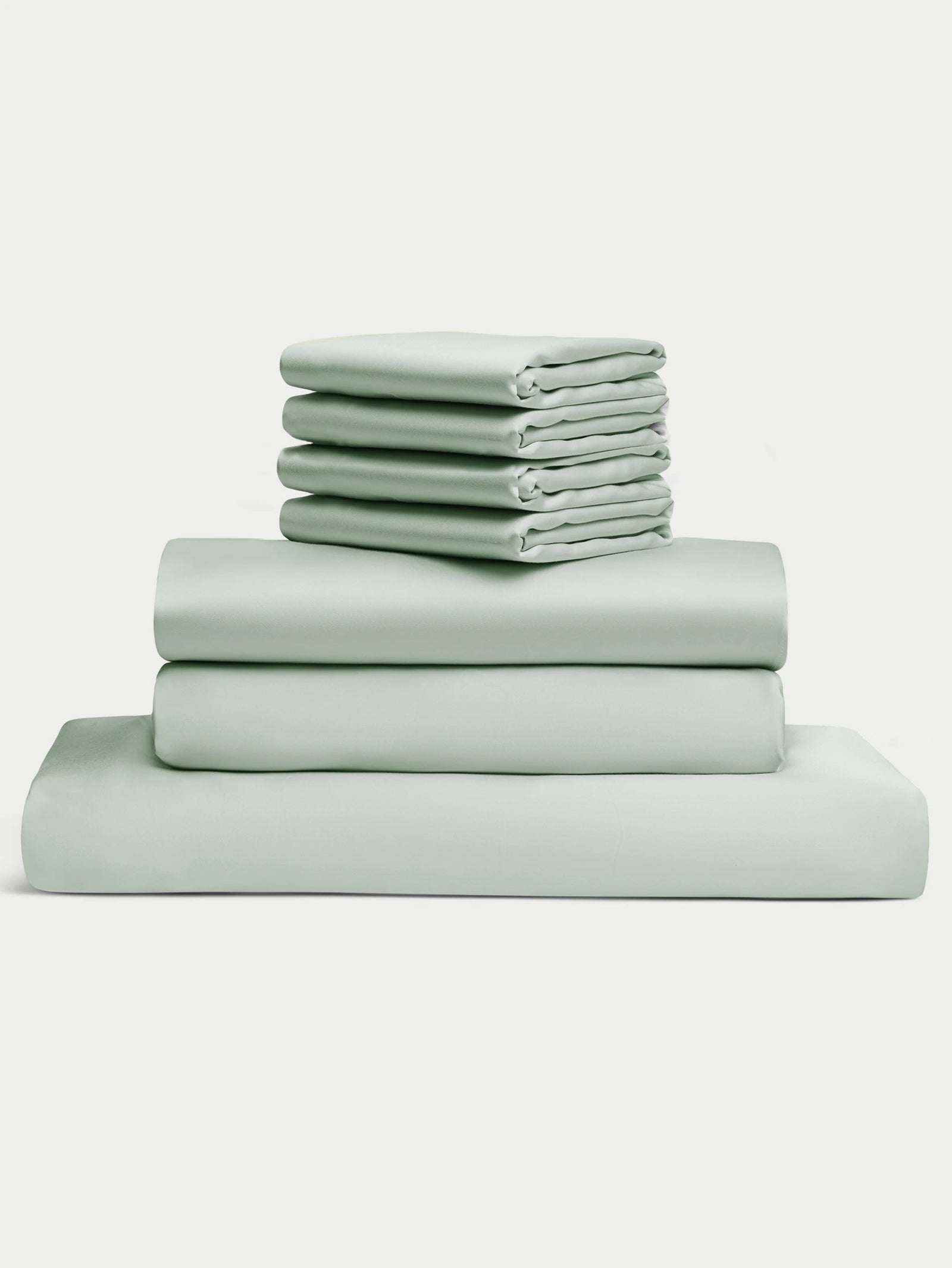 A neatly stacked Bamboo Bedding Core Bundle by Cozy Earth, featuring light green flat and fitted sheets along with pillowcases, arranged on a plain white background. 