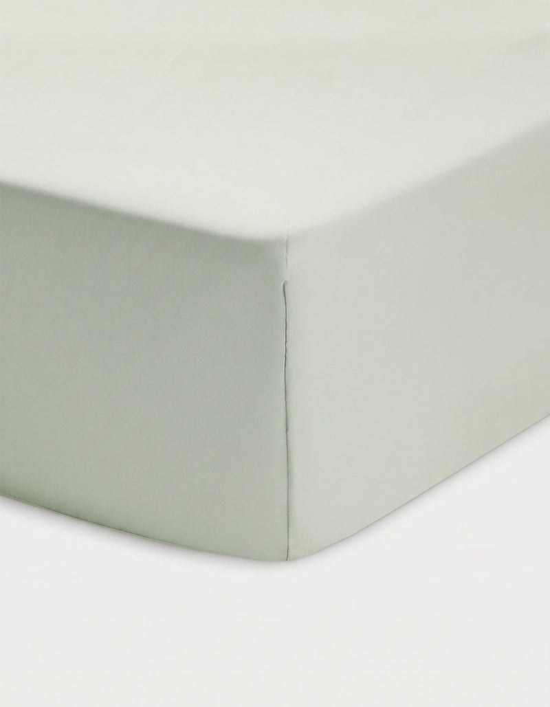 Close-up of a corner of a bed showcasing the Cozy Earth Bamboo Fitted Sheet in light green, neatly covering the mattress against a white background.