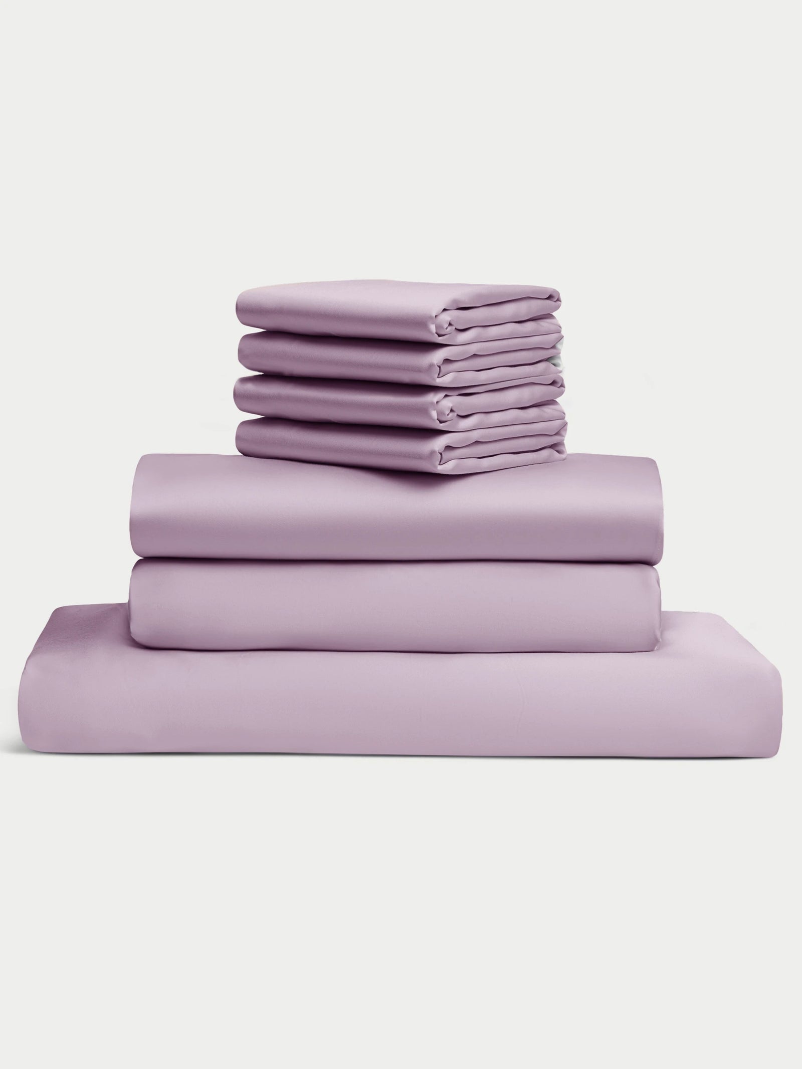 The Bamboo Bedding Core Bundle by Cozy Earth features a neatly stacked set of lavender bed sheets and pillowcases, including a fitted sheet, flat sheet, and four pillowcases, displayed against a plain white background. 