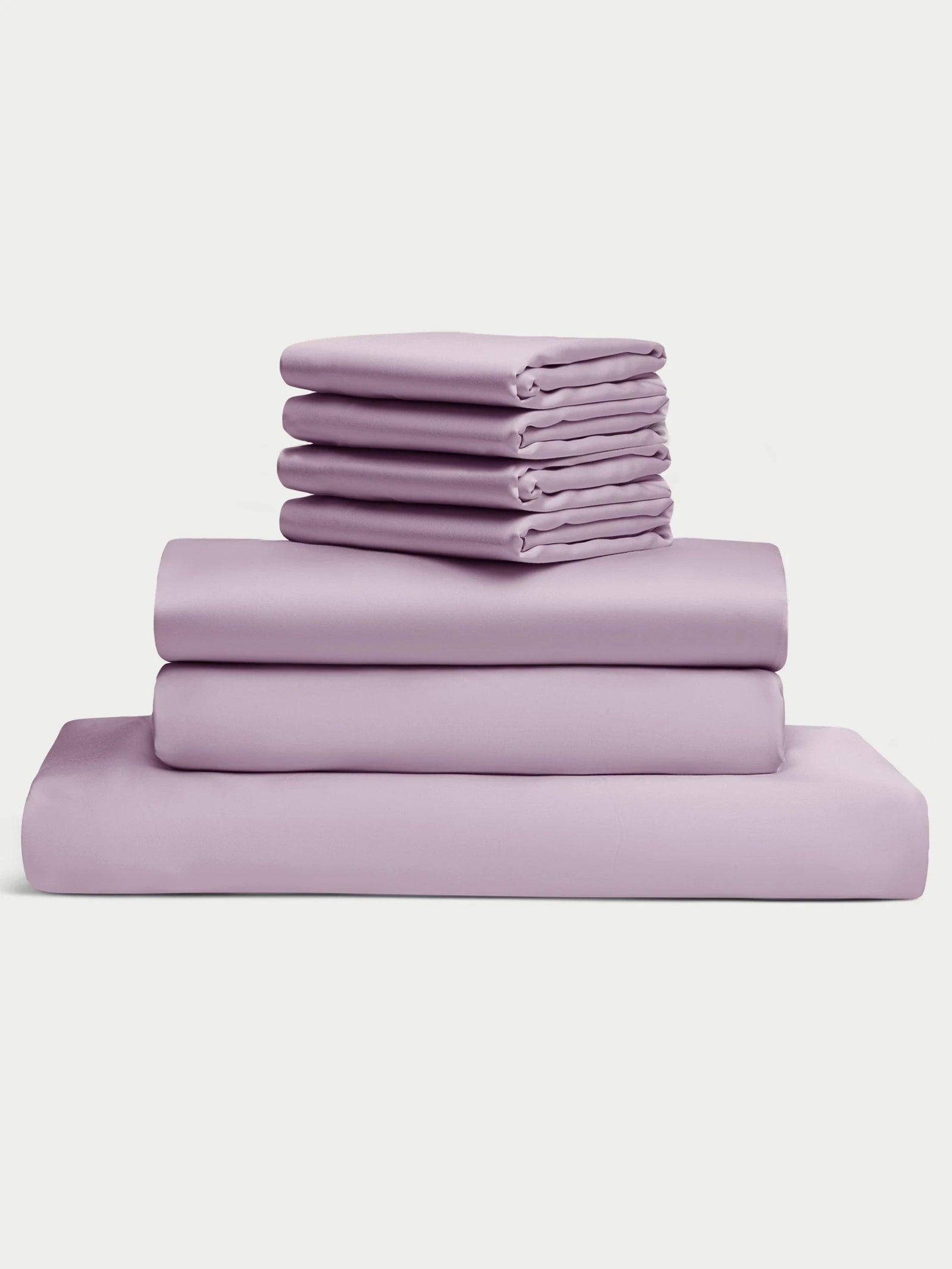 A neatly stacked Bamboo Bedding Core Bundle by Cozy Earth, featuring purple bed sheets and pillowcases, against a plain white background. Multiple folded sheets and pillowcases are arranged in an organized manner. 