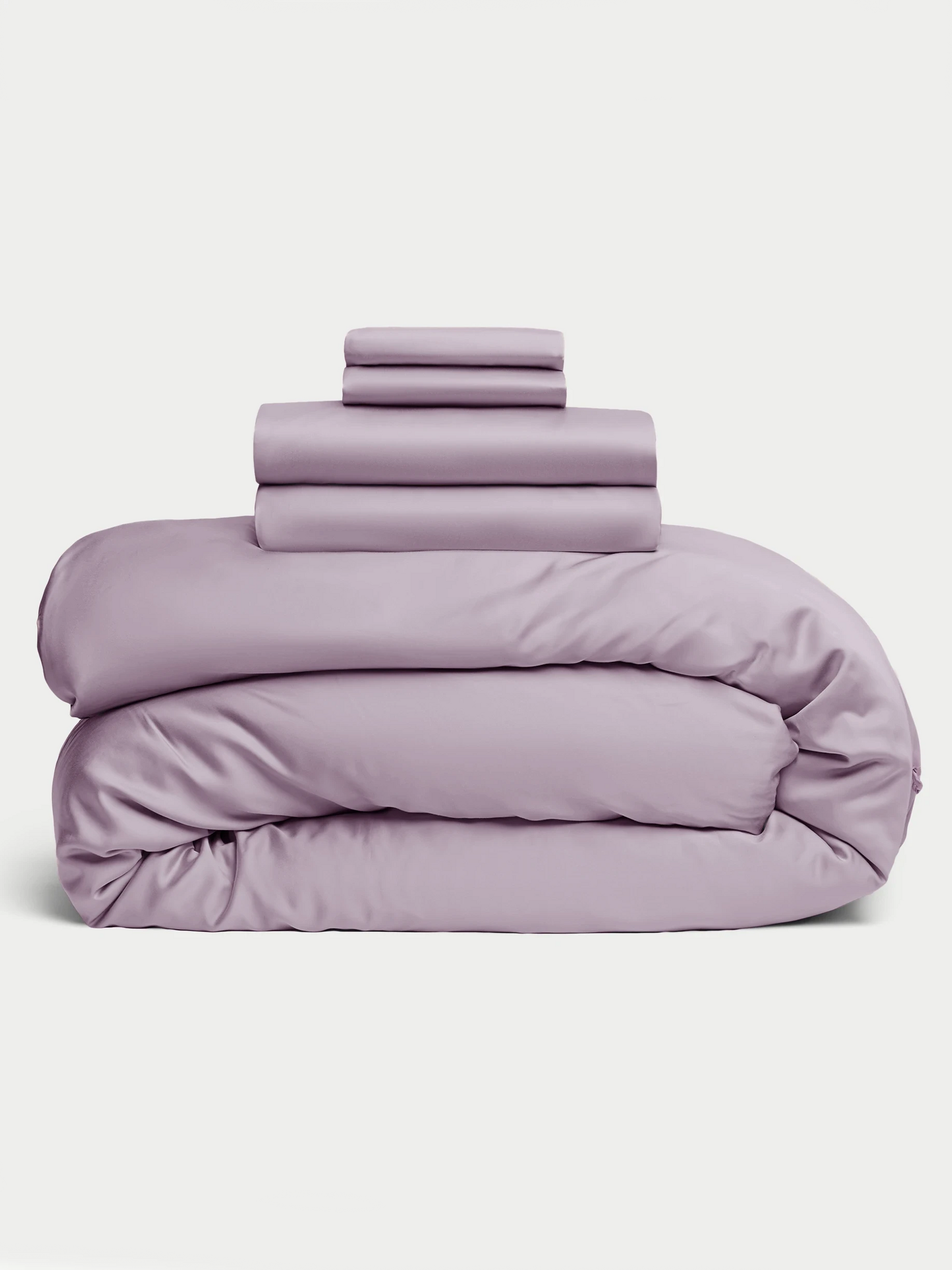 The Cozy Earth Bamboo Bedding Deluxe Bundle, featuring a lavender comforter, sheets, and pillowcases, is neatly folded and stacked against a plain white background. 