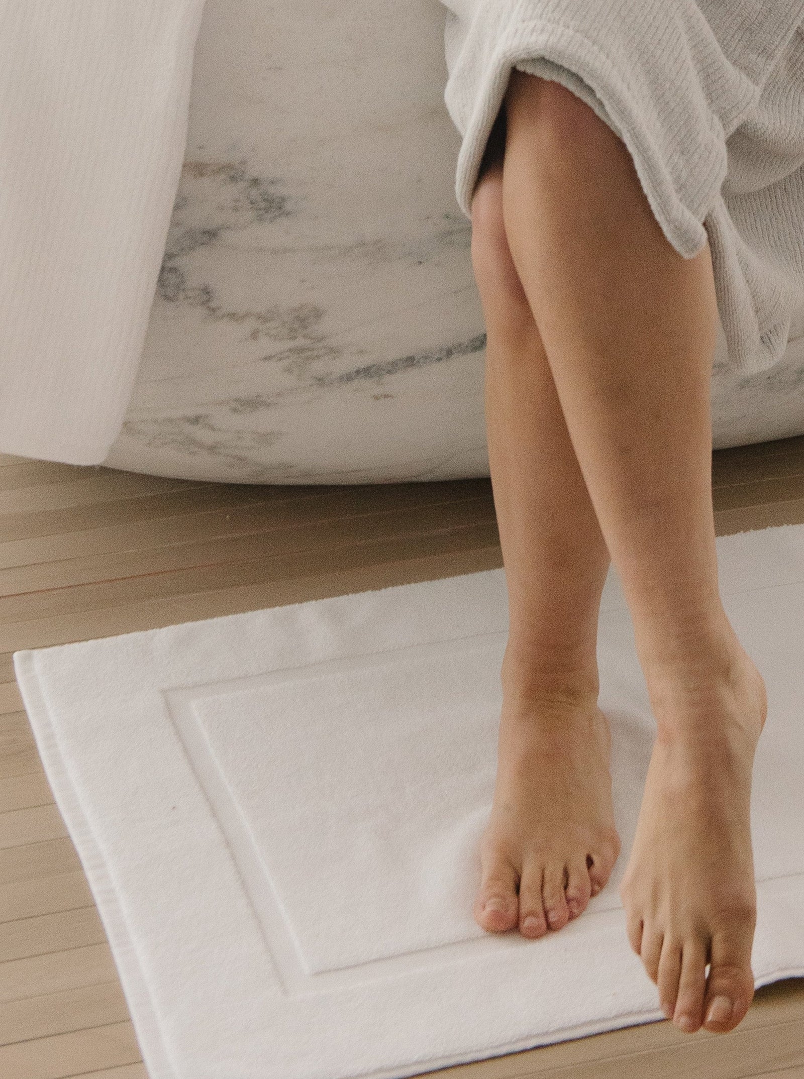 White Premium Plush Bath Mat resting on floor next to bathtub. The photo was taken in a bathroom showing a persons feet resting on the bath mat.