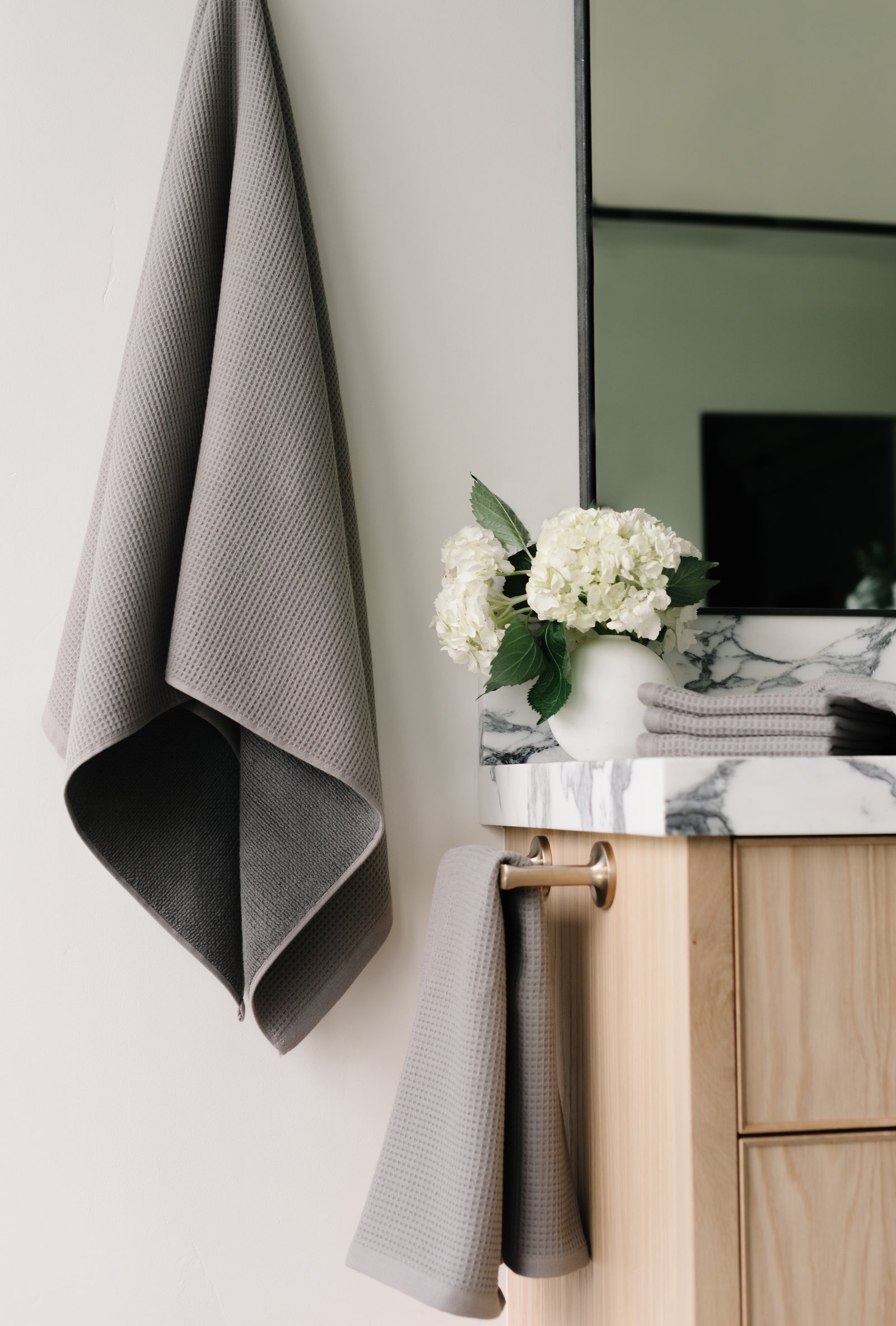 Waffle Bath Towel in the color Charcoal. Photo of Charcoal Waffle Bath Towel taken with Charcoal Waffle Bath Towel hanging from towel hook in a bathroom with white walls 