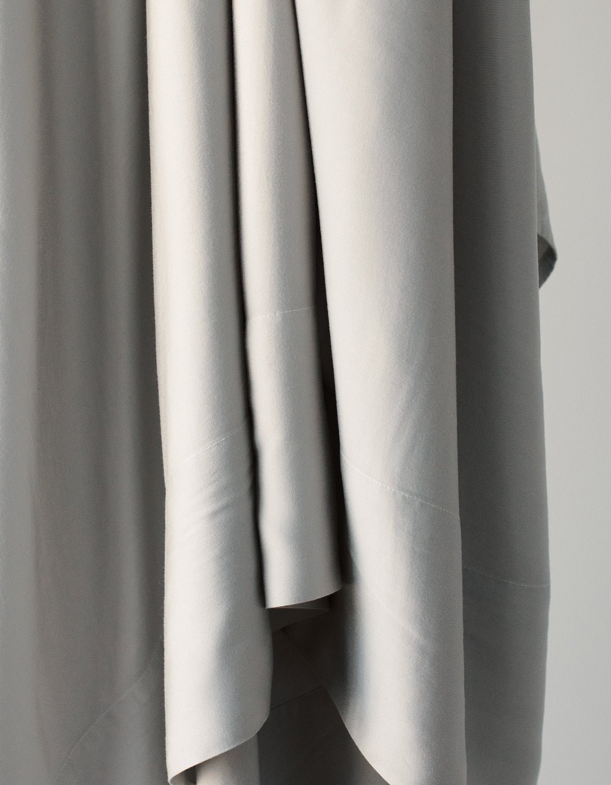 A close-up of the Bamboo Sheet Set by Cozy Earth highlights its soft, light gray fabric draped gracefully, showcasing smooth texture and gentle folds. 
