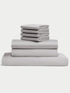The Cozy Earth Bamboo Bedding Core Bundle includes light gray bed sheets and pillowcases, neatly stacked in a pile on a white background.