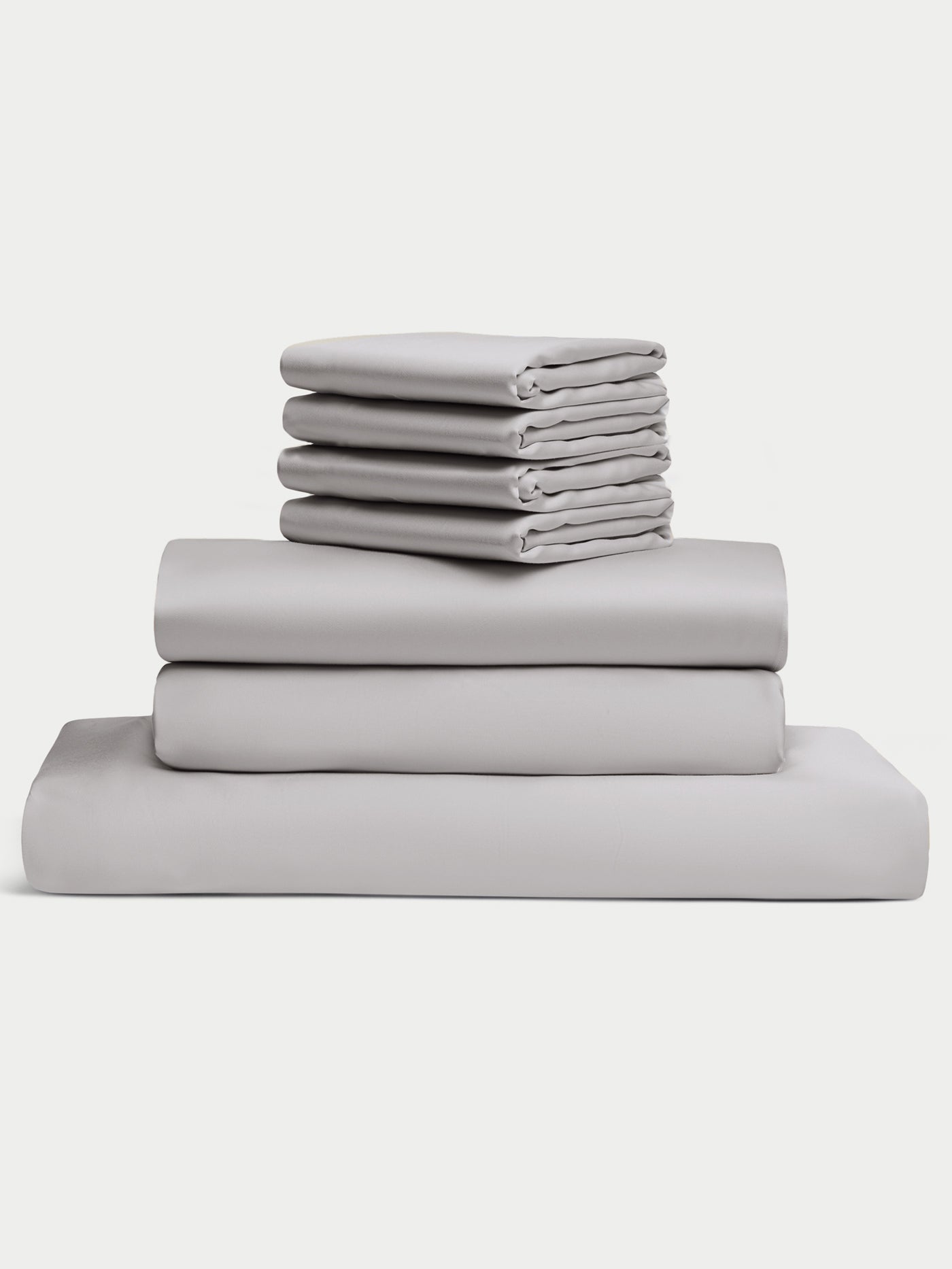 The Cozy Earth Bamboo Bedding Core Bundle includes light gray bed sheets and pillowcases, neatly stacked in a pile on a white background.