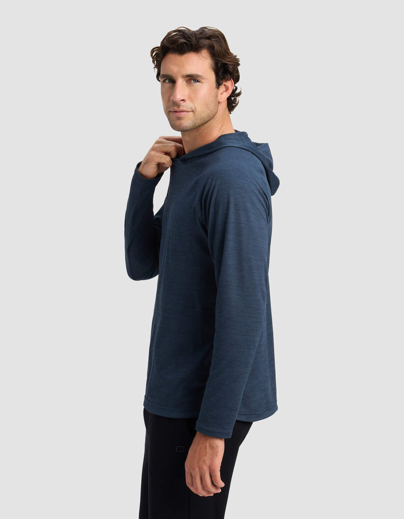 A man in a Cozy Earth Men's Lightweight Performance Hoodie stands sideways against a plain light grey background, turning his head to the camera and touching his collar, wearing black pants.