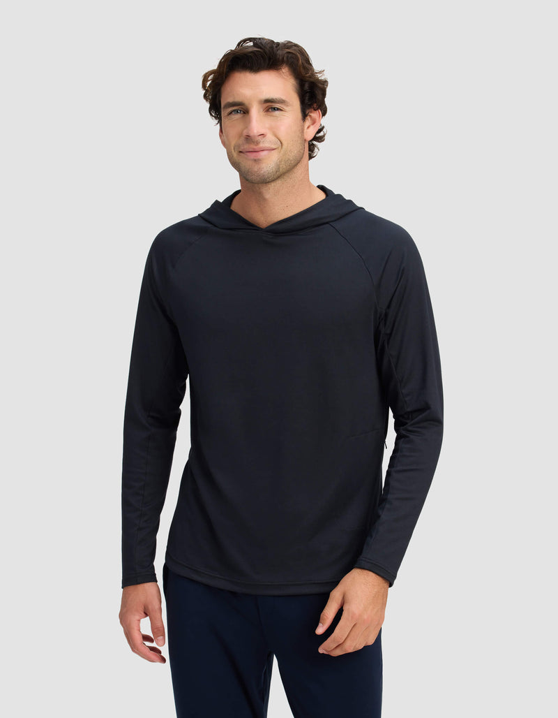 A man with short, wavy brown hair is wearing the Men's Lightweight Performance Hoodie by Cozy Earth, standing against a plain light gray background and smiling slightly at the camera.