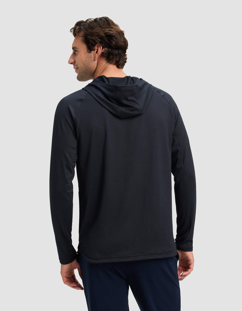 A man with wavy brown hair faces away from the camera, wearing the Cozy Earth Men's Lightweight Performance Hoodie in black and navy pants against a plain light gray background.