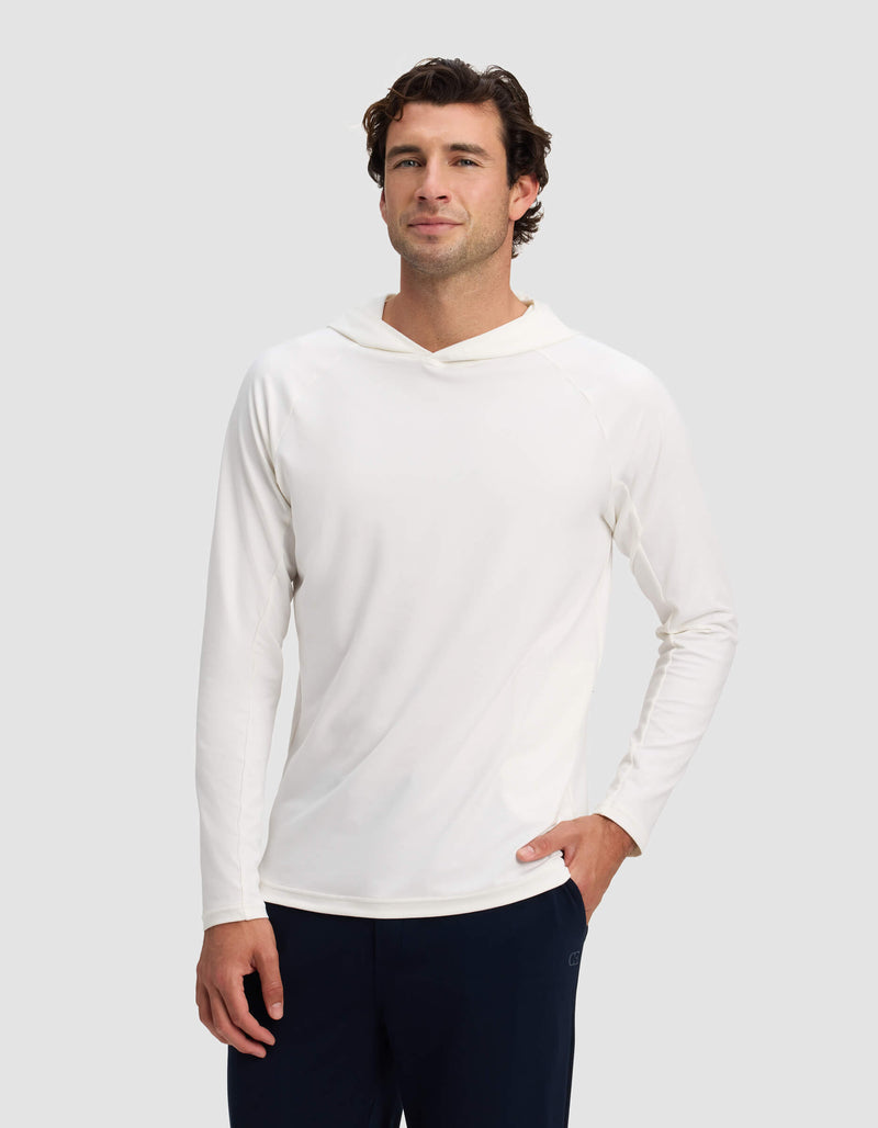 A man wears the Cozy Earth Men's Lightweight Performance Hoodie in white with dark pants, standing against a light gray background, facing forward with one hand in his pocket and a slight smile.