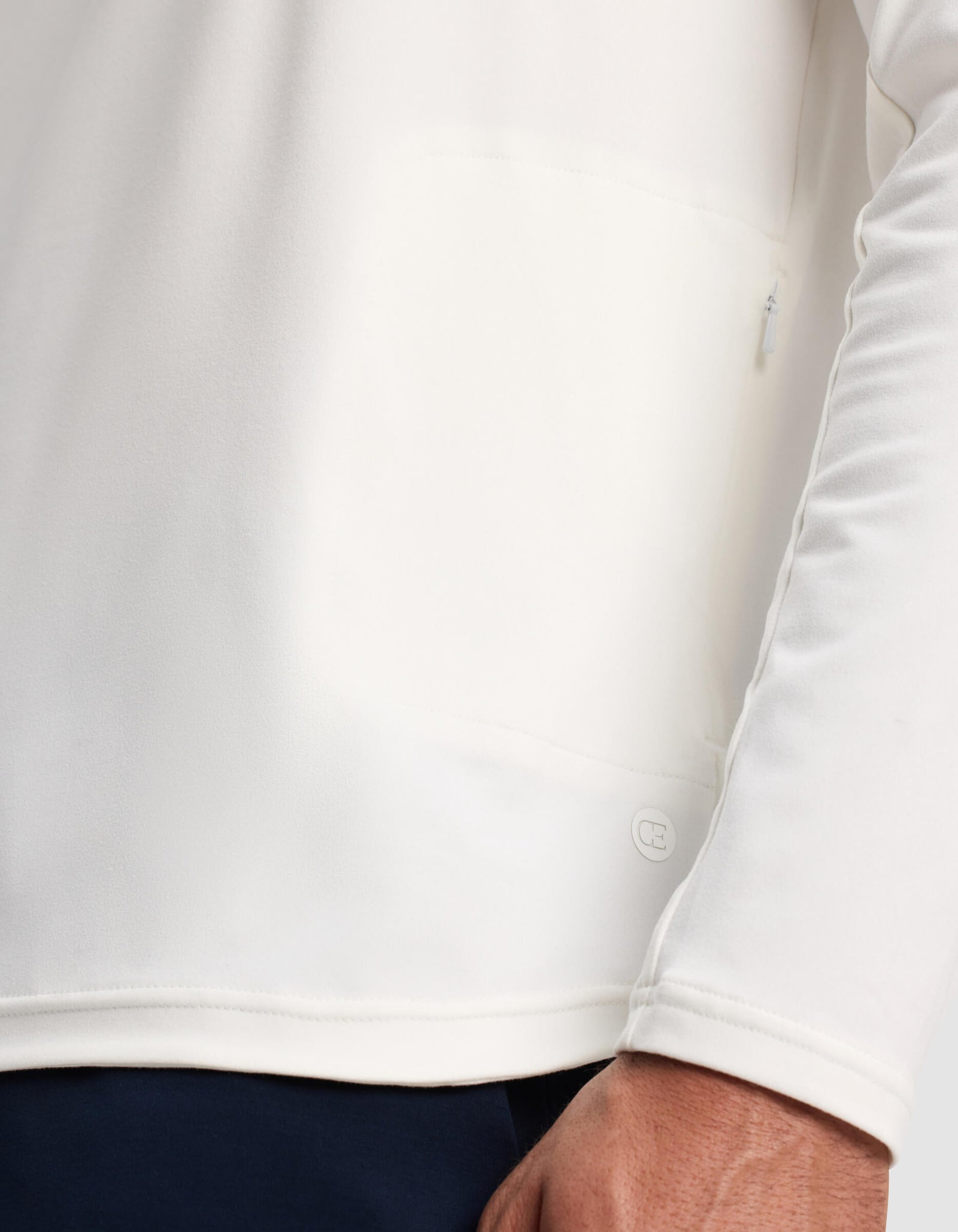 A close-up of a person wearing the Cozy Earth Men's Lightweight Performance Hoodie in white, highlighting the lower hem, a small logo detail, and part of the person's hand.