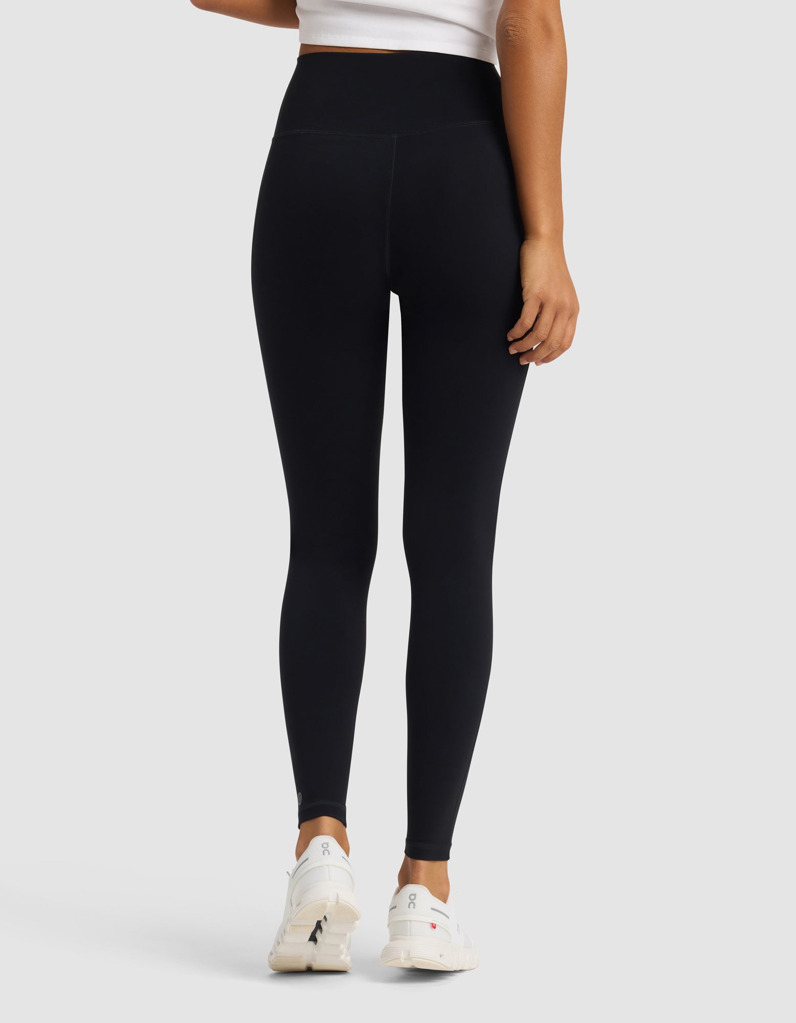 A person, seen from behind against a light gray backdrop, is wearing Cozy Earth's Women's Liv Legging in black paired with a white crop top and white athletic shoes.