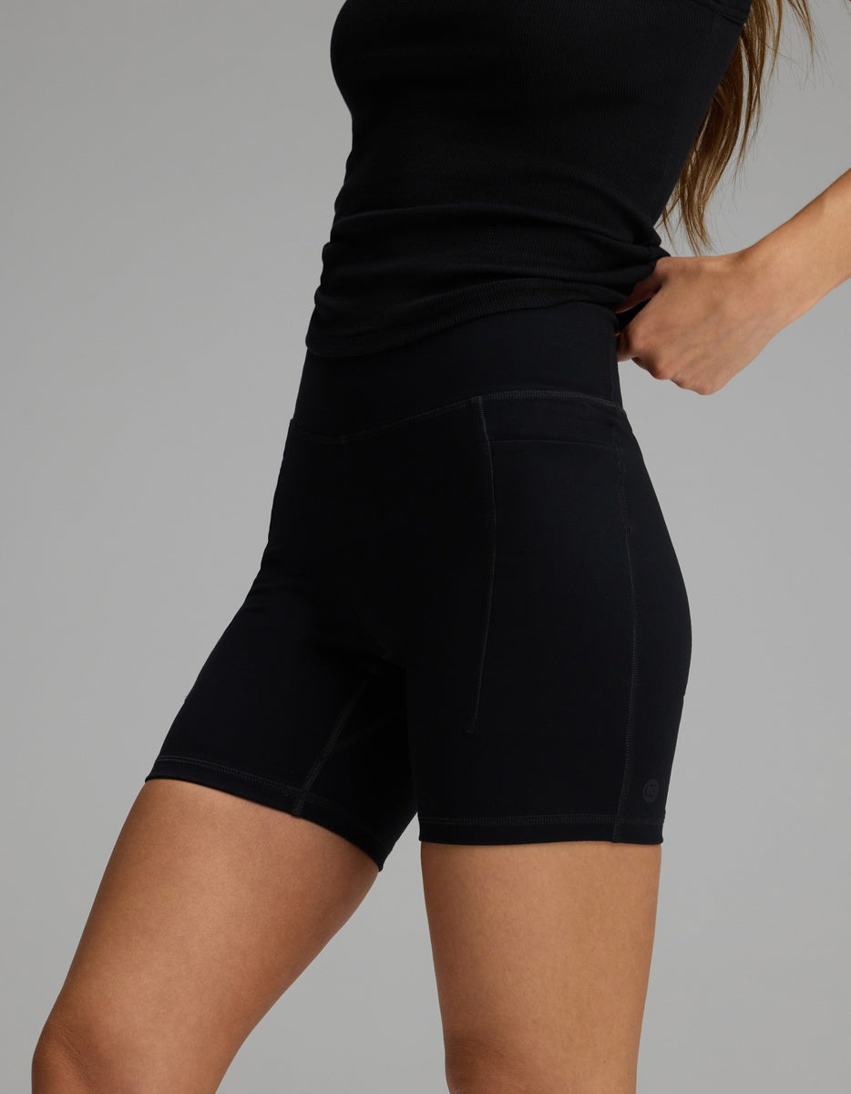 A person wearing black Women’s Liv Biker Short 6″ with Pockets, featuring a high-waisted fit and side pockets.