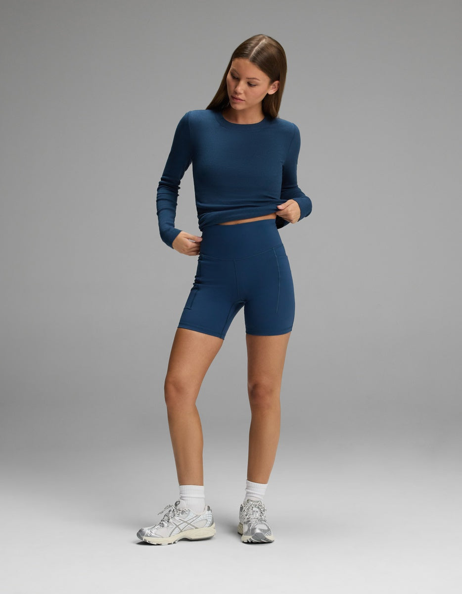 A person wearing a long-sleeved blue top and matching blue Women’s Liv Biker Short 6″ with Pockets.