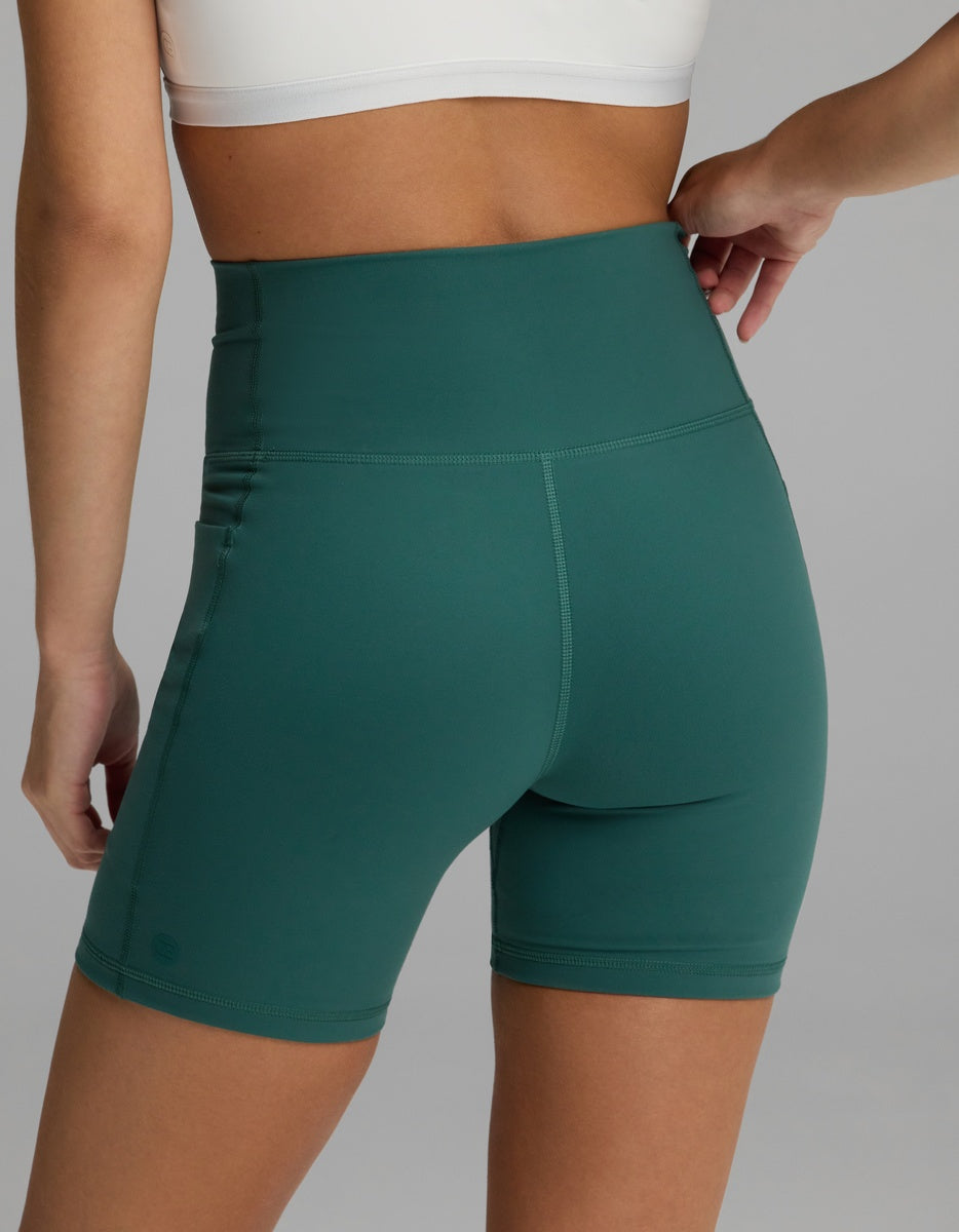 Rear view of dark green Women’s Liv Biker Short 6″ with Pockets featuring a high-waisted design and side pockets.