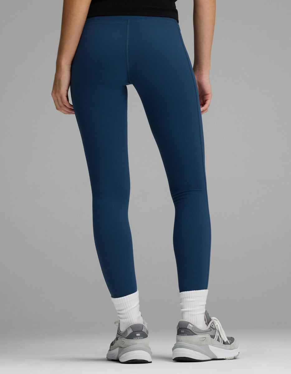 Rear view of a person wearing solid blue Women’s Liv Leggings, white crew socks, and grey athletic sneakers.