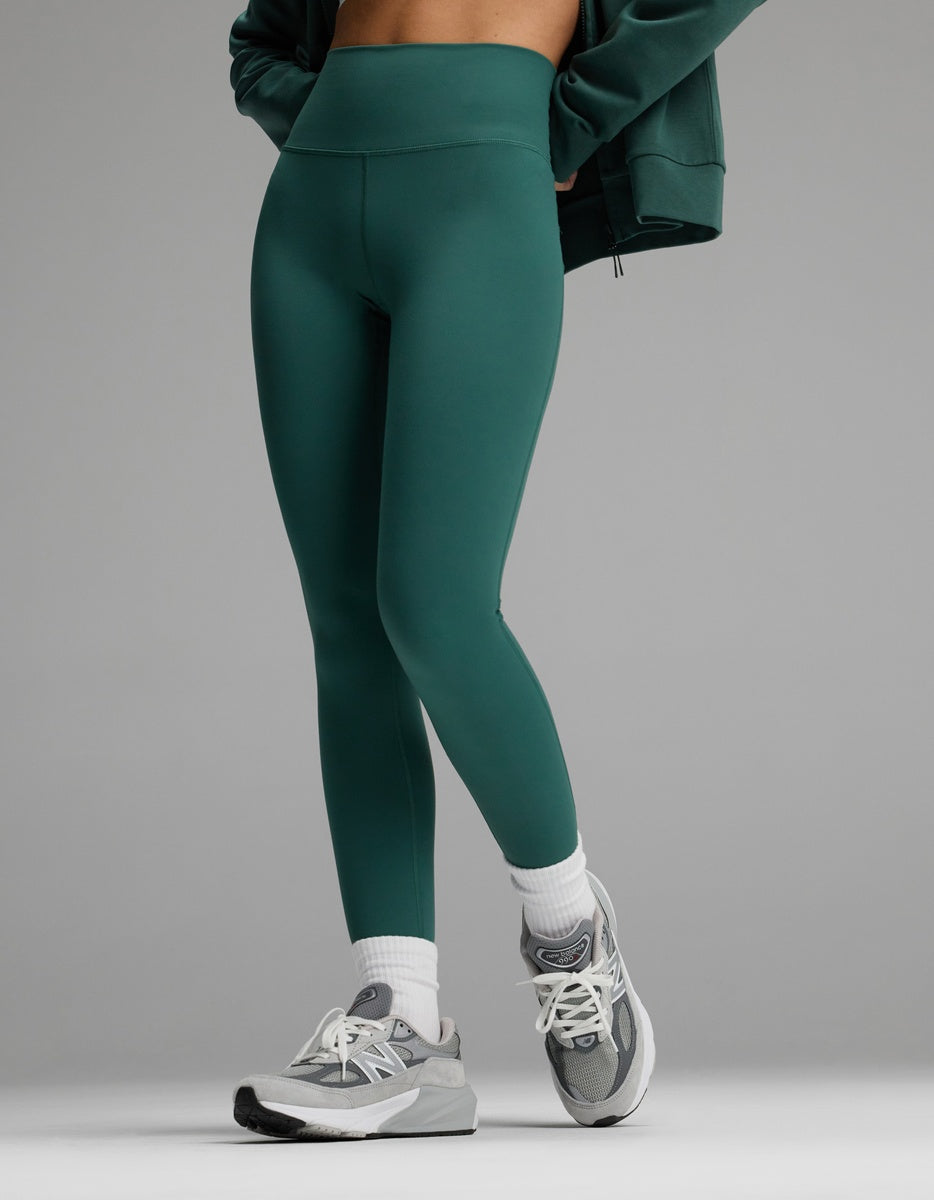 A person wearing dark green Cozy Earth Women’s Liv Leggings, white socks, and grey athletic sneakers.