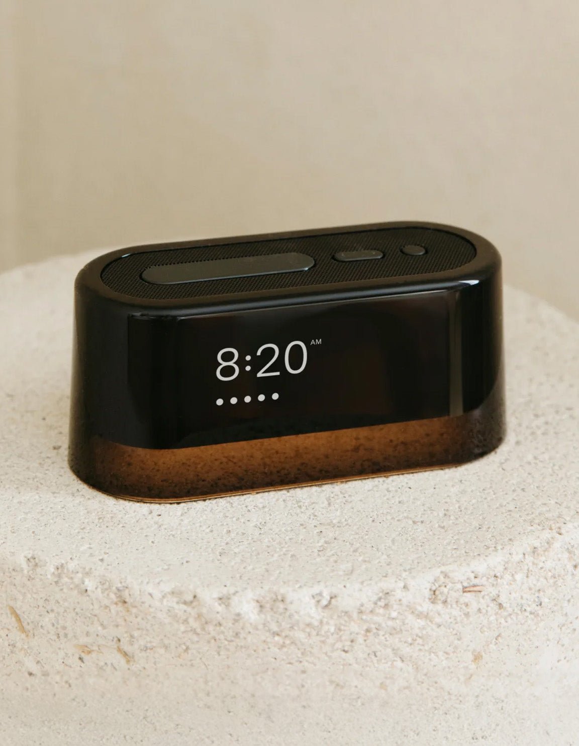 The Cozy Earth Bamboo Sheet Set x Loftie Clock features a sleek, black, rounded digital alarm clock showing 8:20 AM on a light stone surface with a beige background.