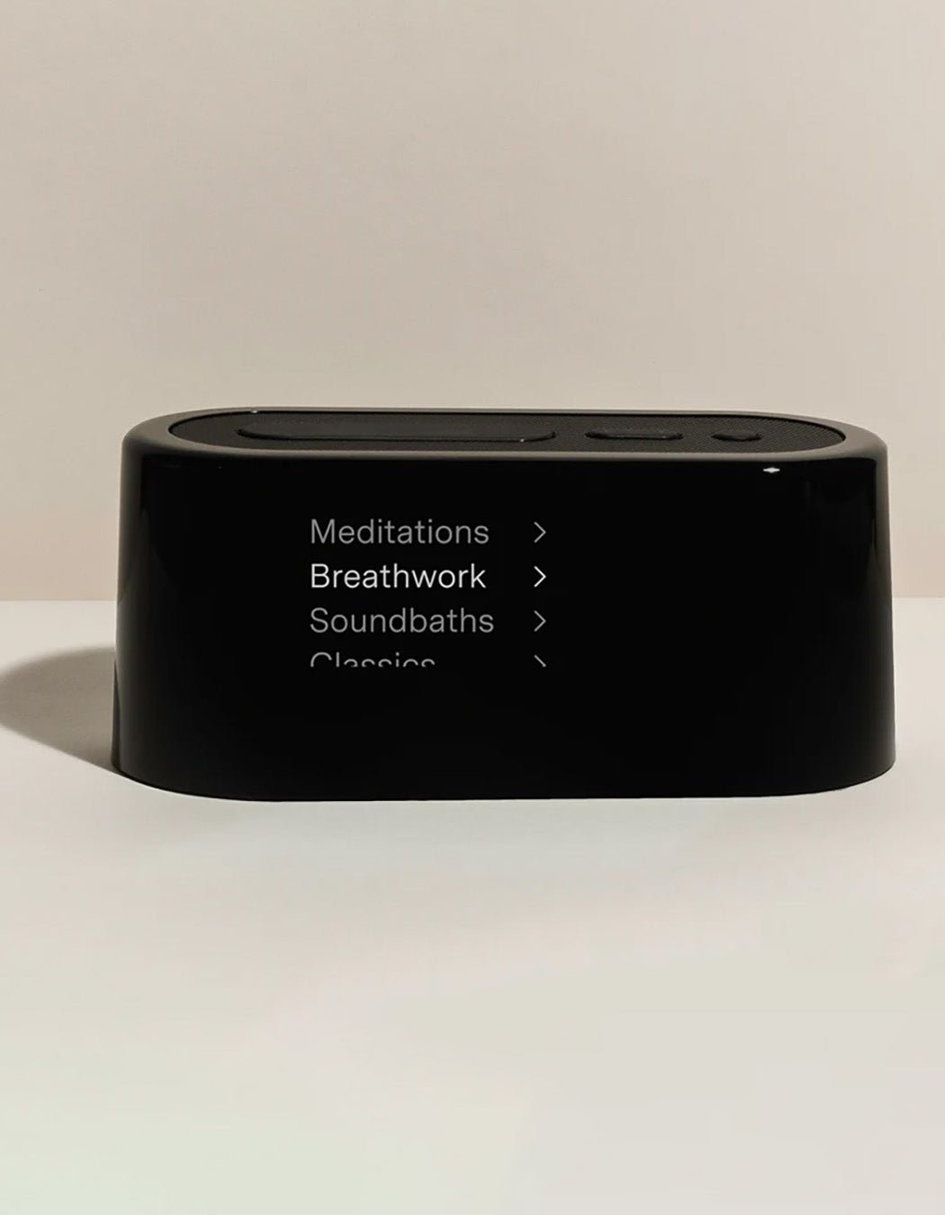 The Cozy Earth Bamboo Sheet Set x Loftie Clock is a black rectangular device with rounded edges showing menu options—Meditations, Breathwork, Soundbaths, and Classics—each marked with a right-pointing arrow.