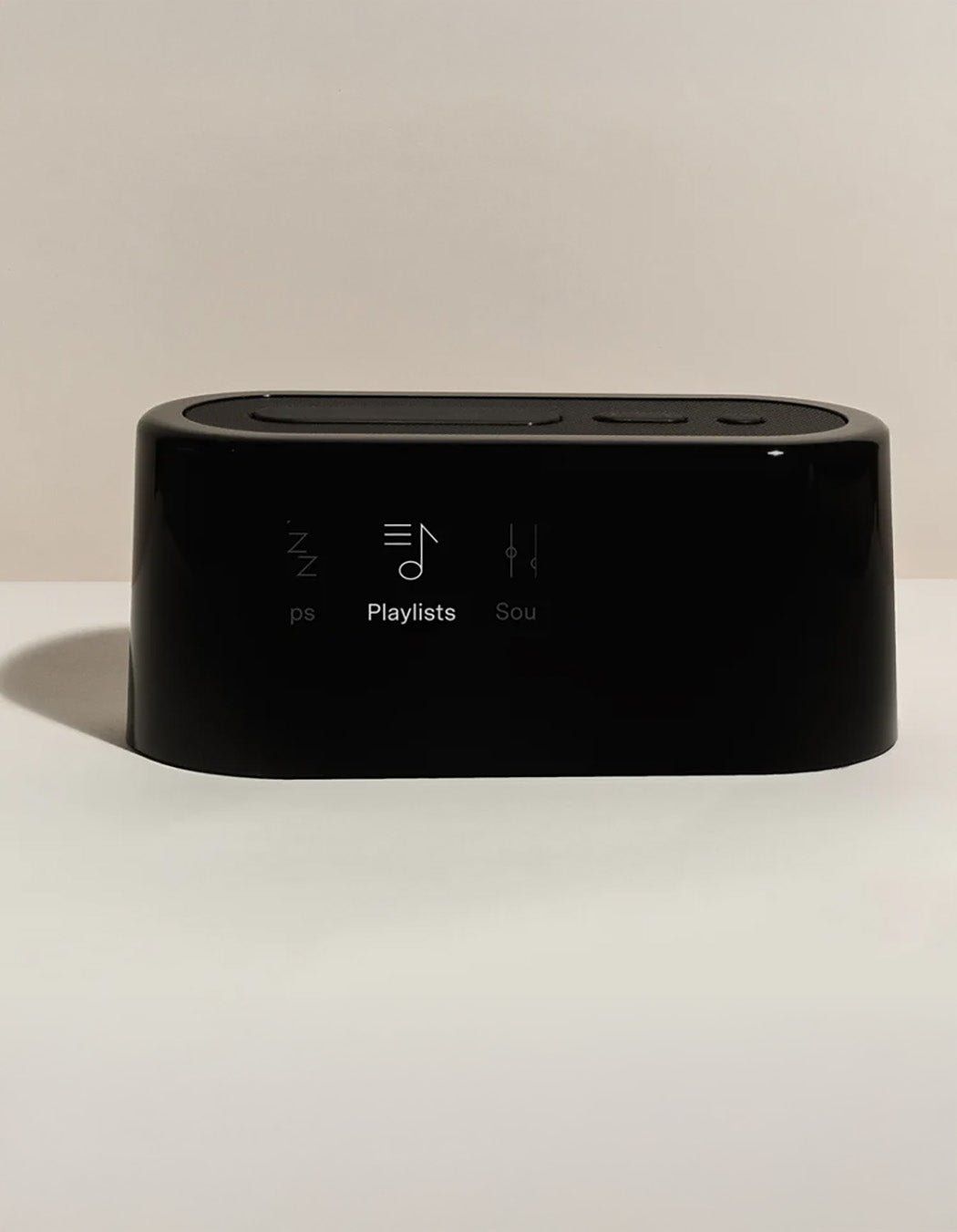 The Cozy Earth Bamboo Sheet Set x Loftie Clock features a sleek black rectangular smart speaker with touch controls and playlist, sleep, and sound setting icons on the front, displayed against a neutral background with soft shadows.