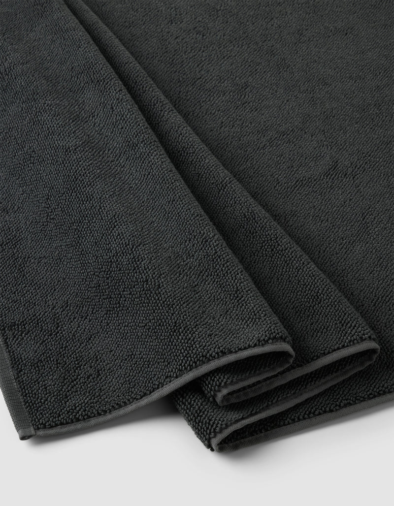 A close-up of the Cozy Earth Loop Terry Bath Mat, neatly folded in dark gray with a soft, textured surface, displayed on a light-colored background.